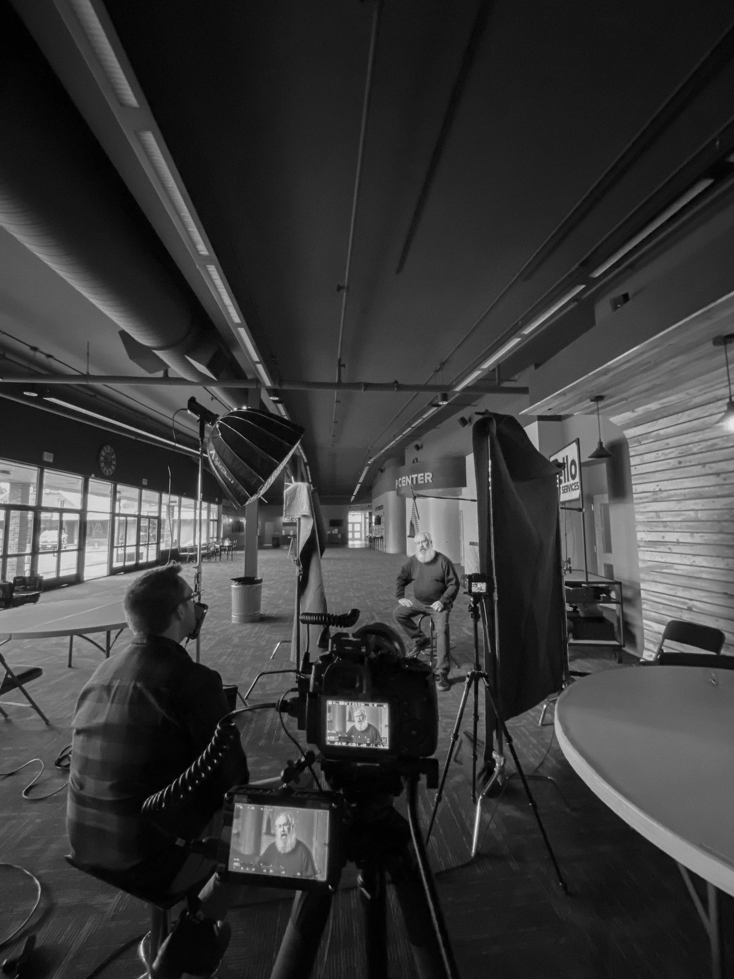 A video production set in Lynden, Washington featuring talent sitting in a chair with a microphone, lights, and cameras being interviewed by someone sitting in a chair.