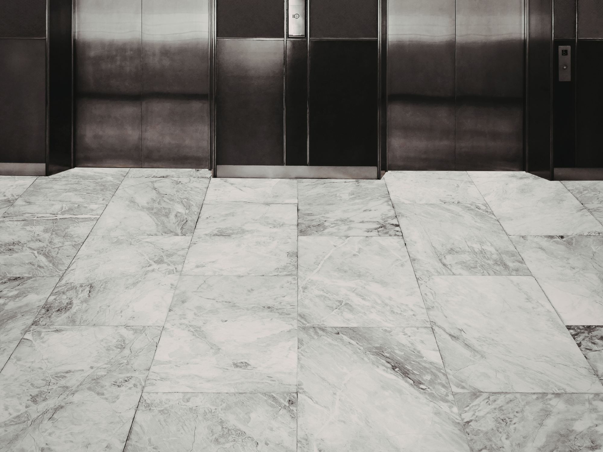 View of two elevator doors in a building lobby with marble tile flooring.