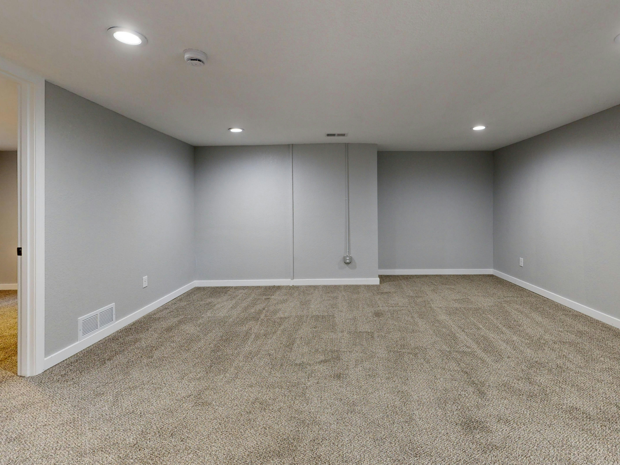 Empty room with gray walls, beige carpet, white baseboards, and recessed ceiling lights.