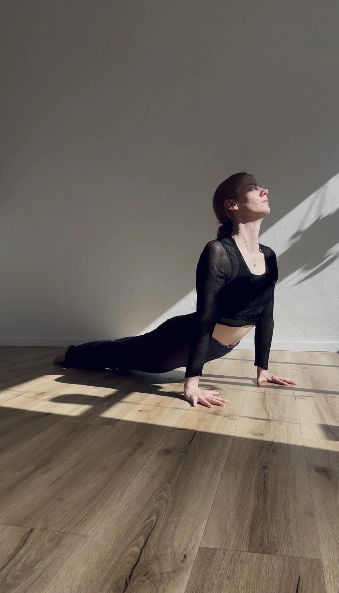 Frau in schwarzer Sportkleidung macht Yoga im Raum, in der Balancierposition auf Händen und Füßen.