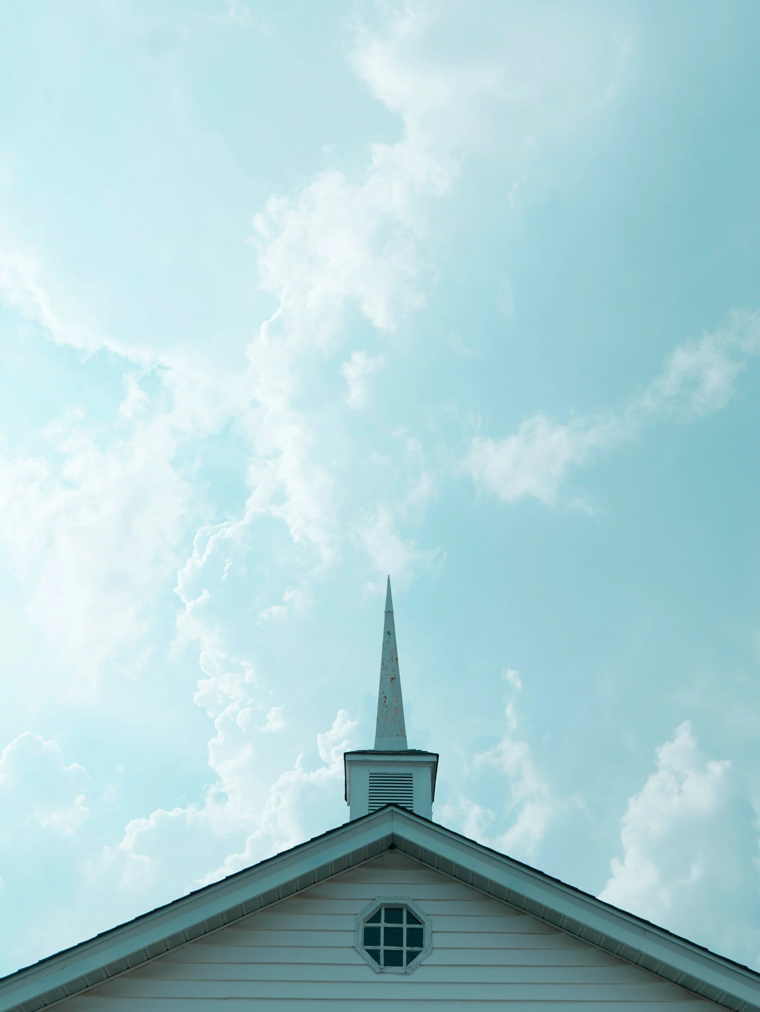 White church steeple on clapboard building under partly cloudy blue sky, photographed by Aaron Burden.