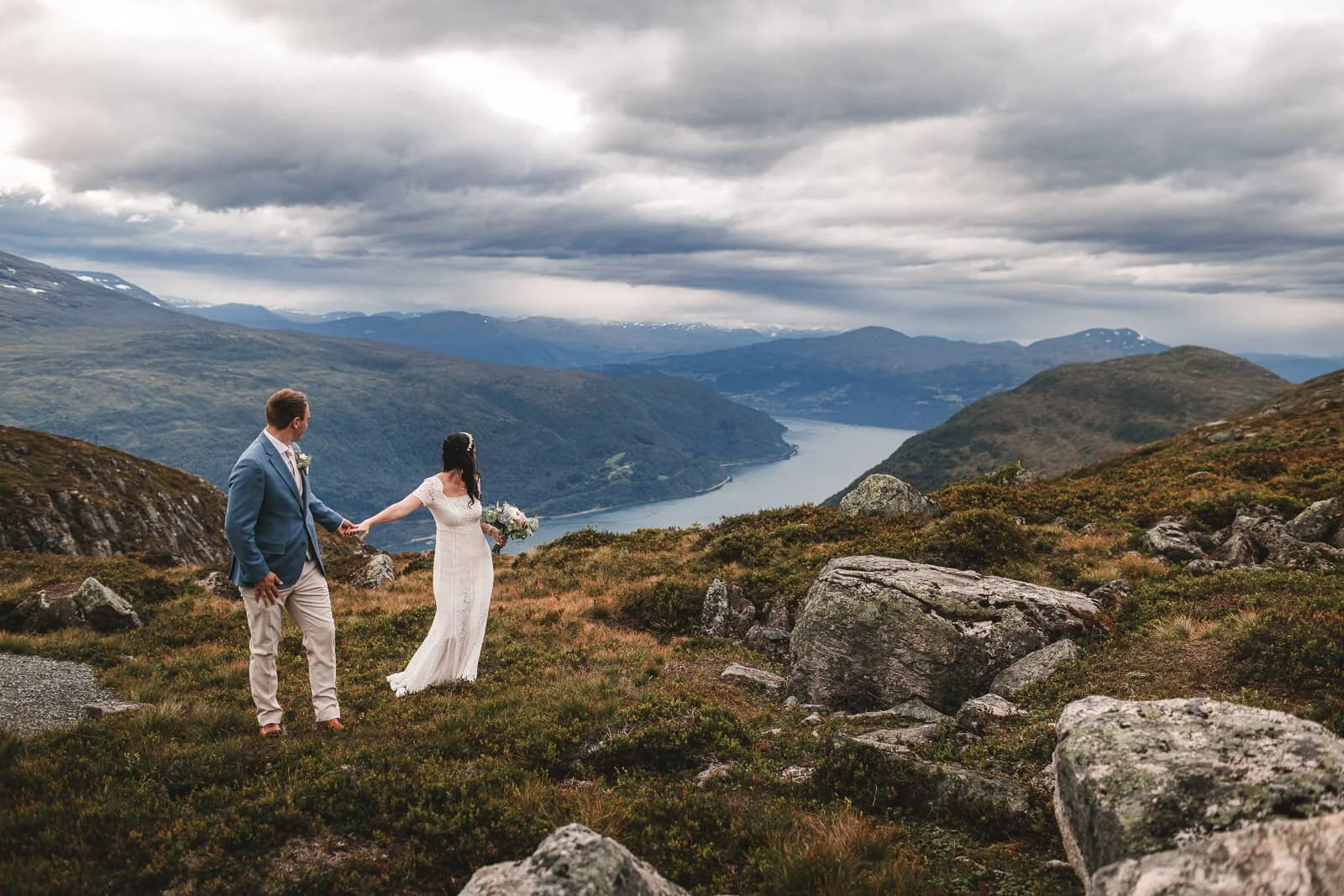 Elopement Norway: a newlywed couple holding hands against the backdrop of the fjords, destination wedding photography by Cécile