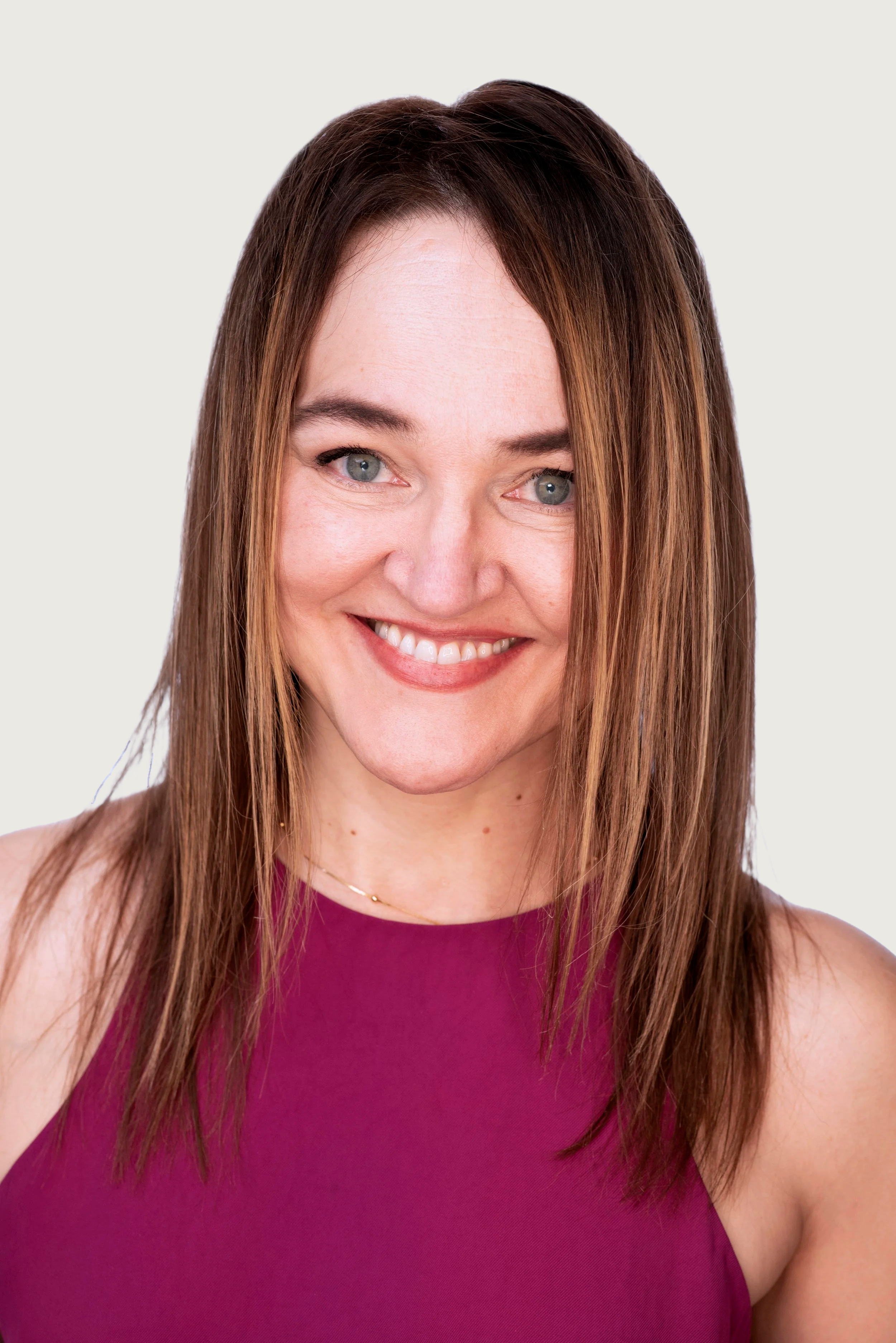Close-up of a woman's smiling face, wearing a sleeveless magenta top, with long brown hair and bright eyes.