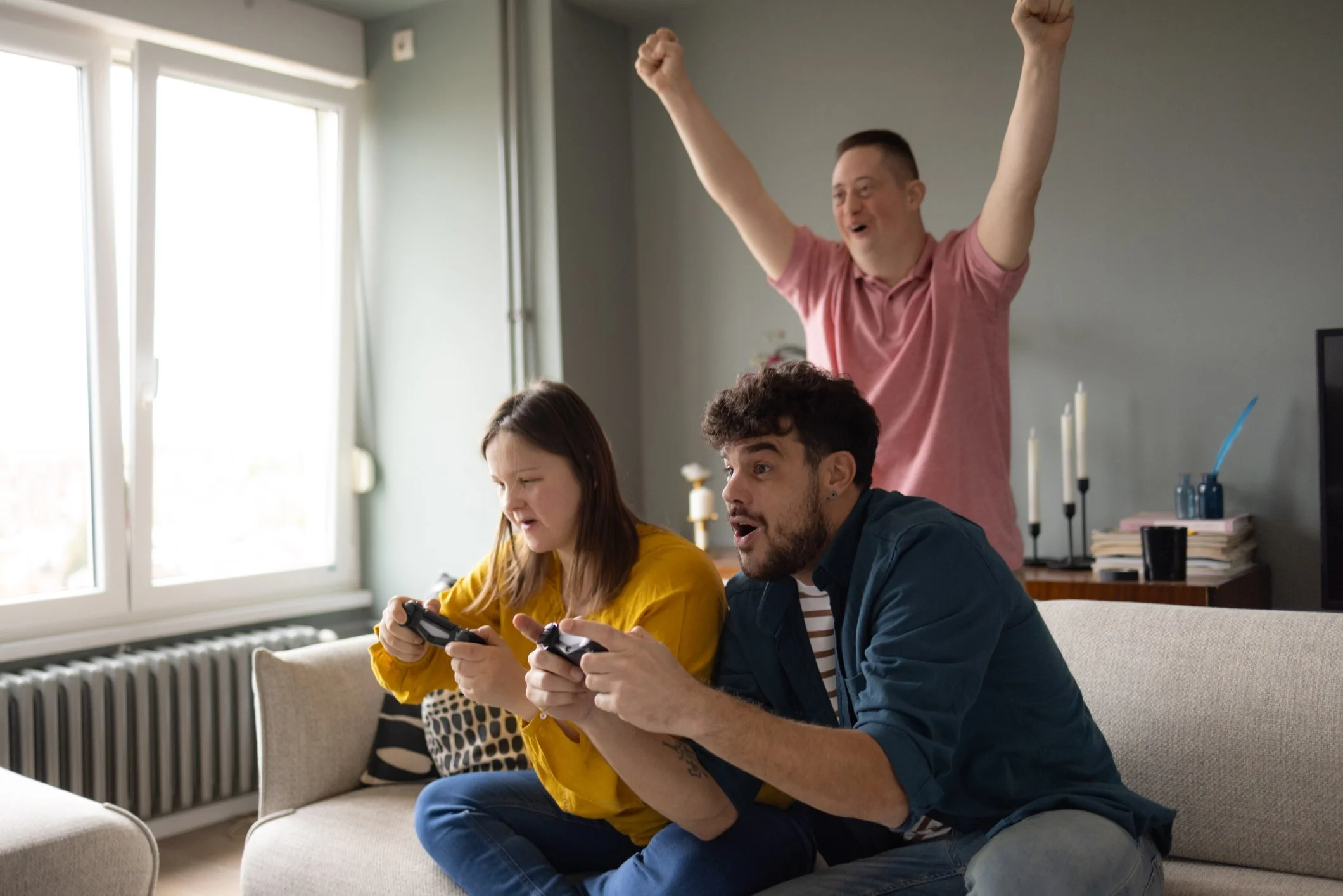 Three friends playing video games, cheering, and celebrating in a living room.
