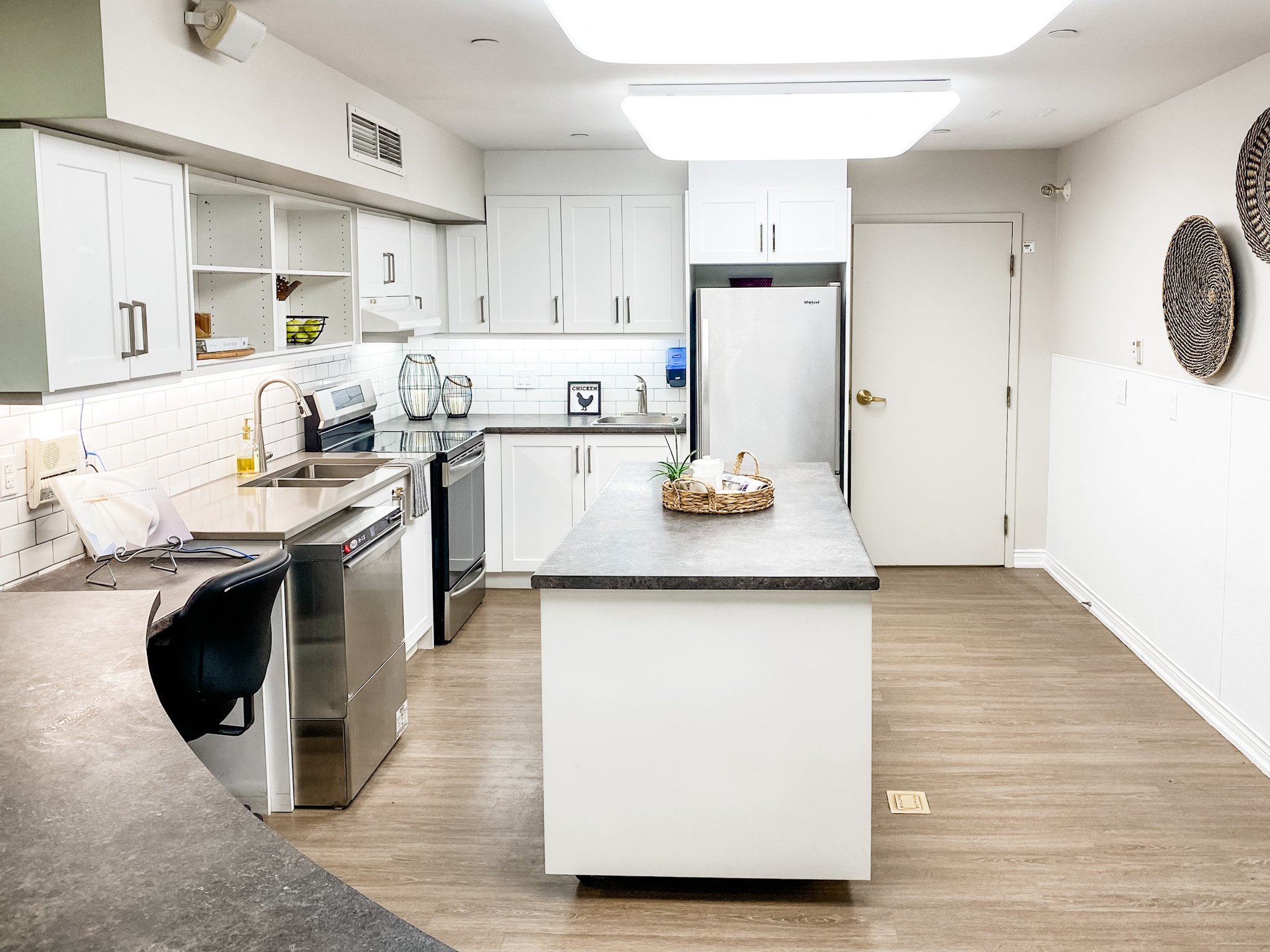 Modern kitchen with white cabinets, stainless steel appliances, a kitchen island, open shelves, and decorative baskets on the wall.