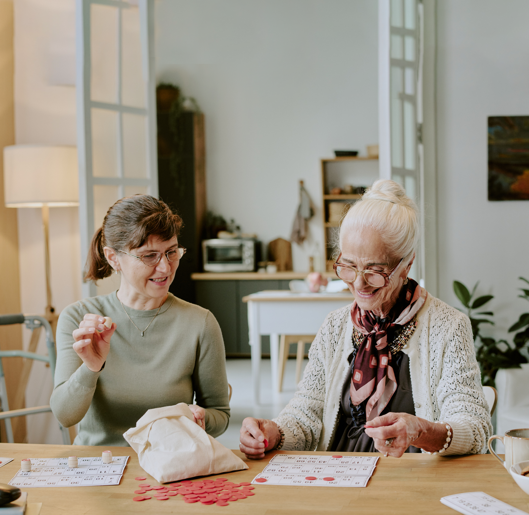 Two women sitting at a table playing bingo, smiling and enjoying each other's company.
