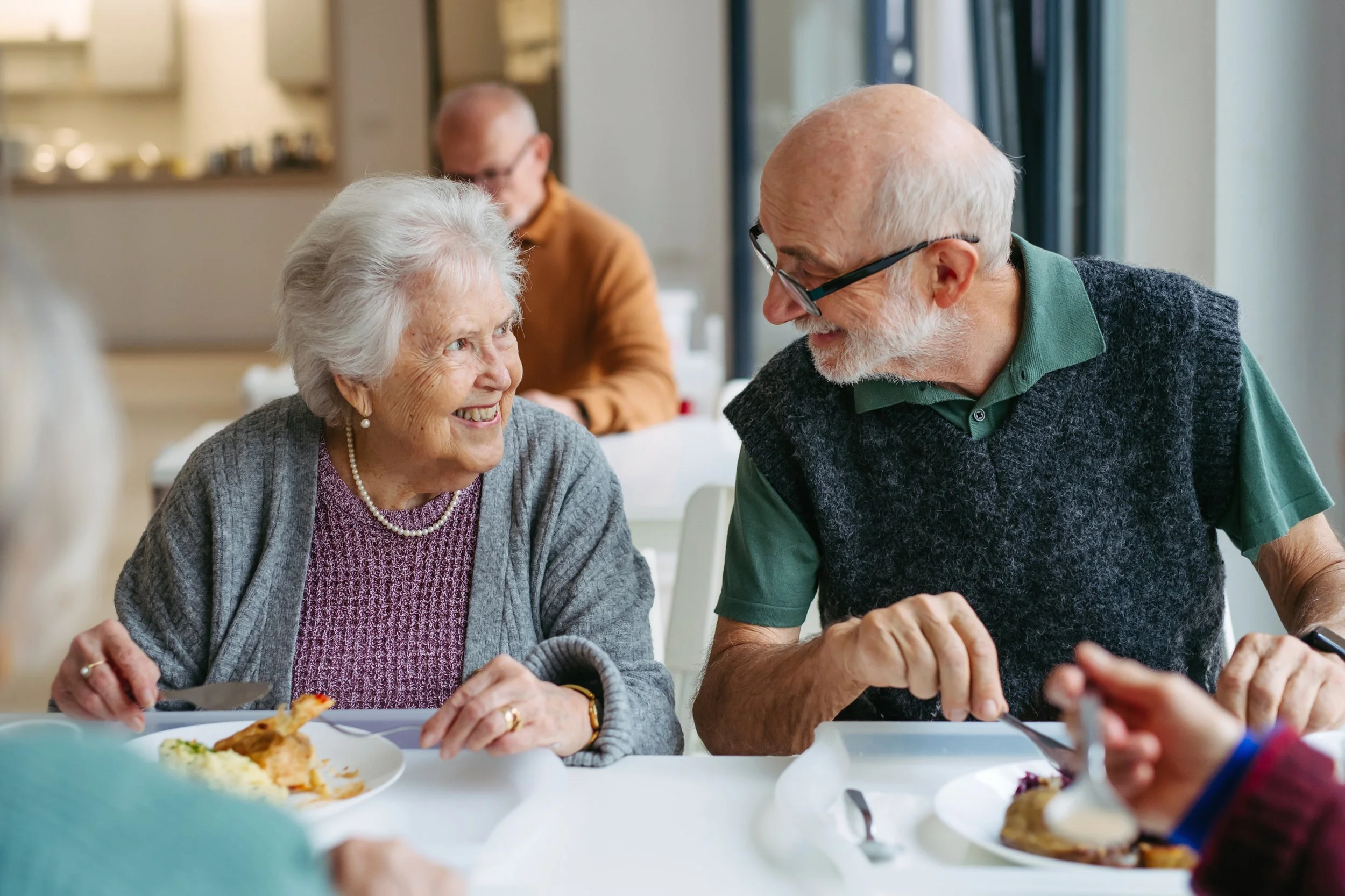 An elderly woman and man smiling and talking during a meal at a restaurant.