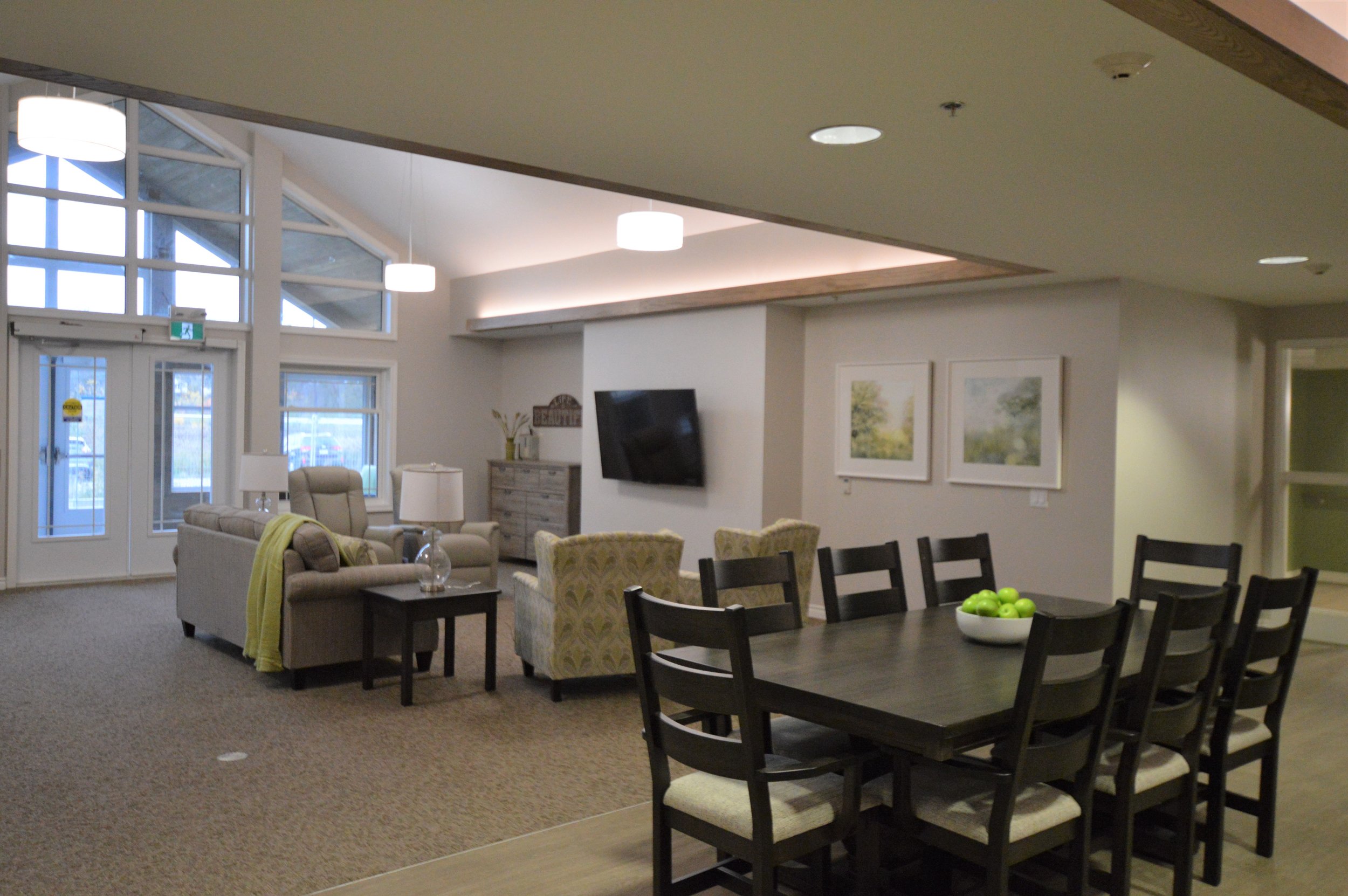 Interior of a modern living room and dining area with a large window, beige sofas, a dark wooden dining table with chairs, and wall art.