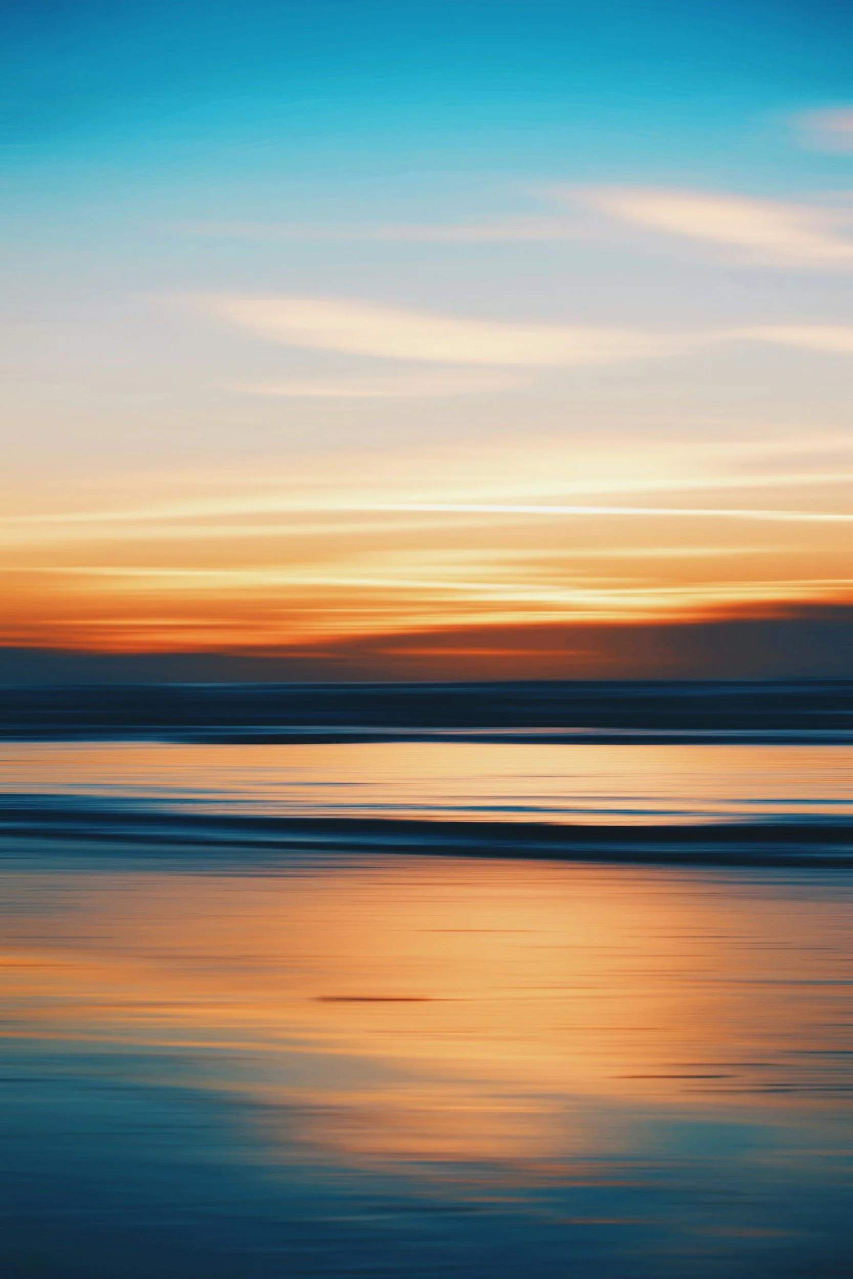 A sunset over the ocean with orange, yellow, and blue sky, and the reflection of the sunset on the water.