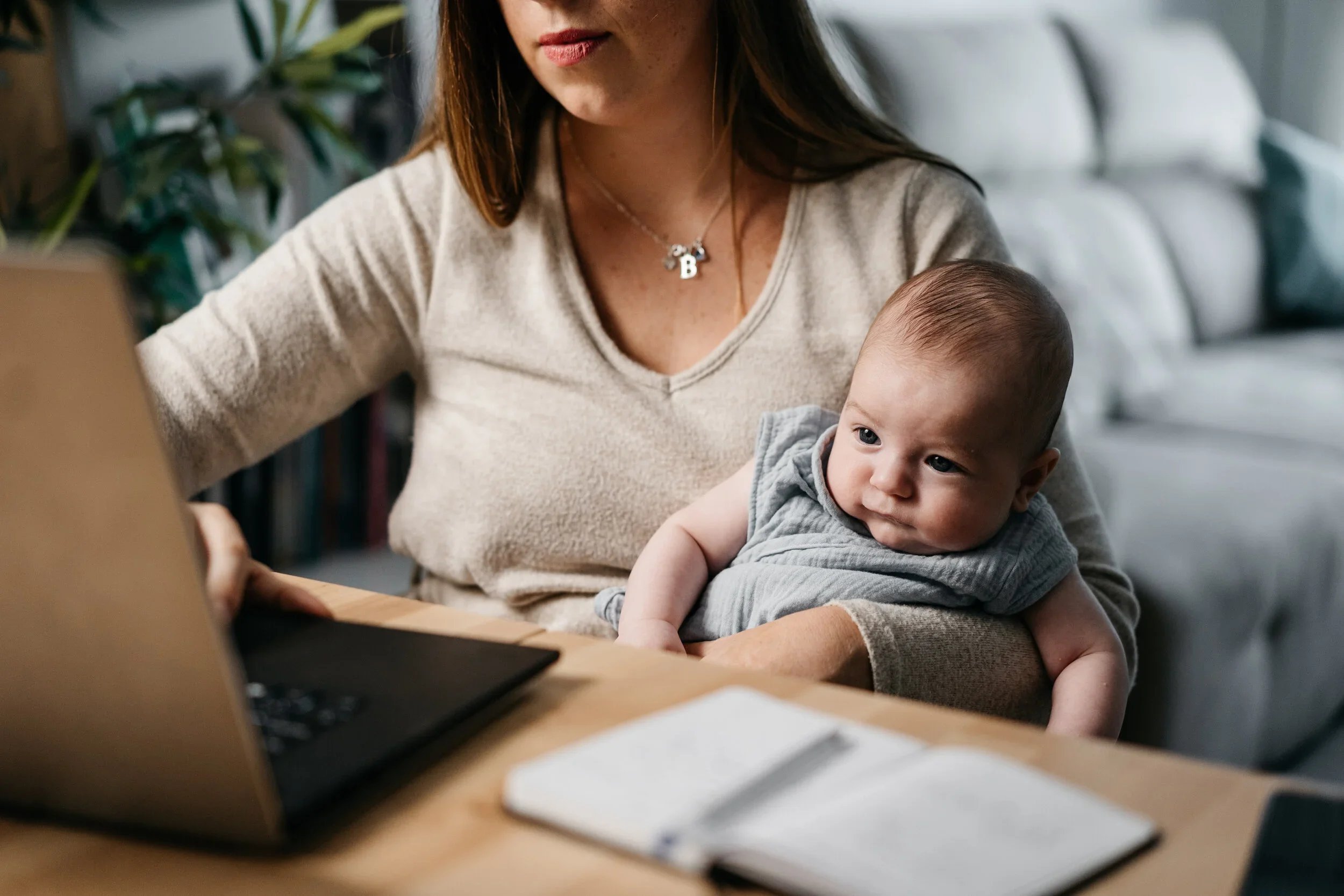mother holding baby and working on her computer.