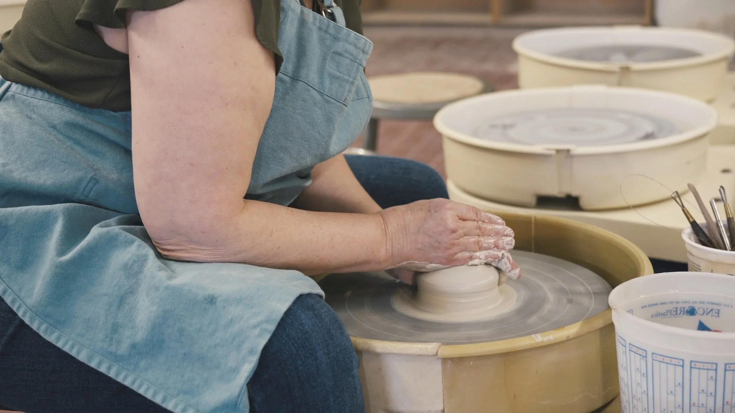 Potter working at a wheel with an ergonomic studio setup focused on body mechanics.