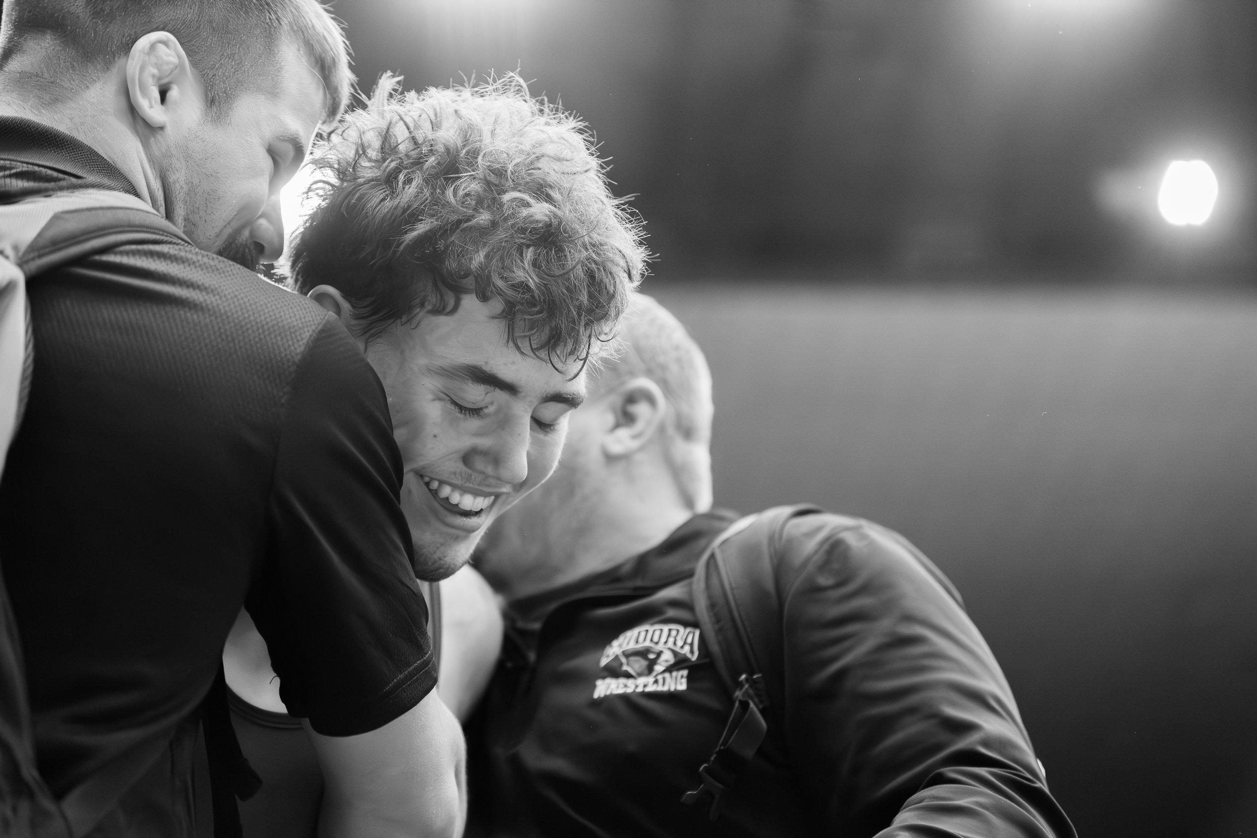 Four smiling young men with athletic clothing on, sharing a happy moment close together.