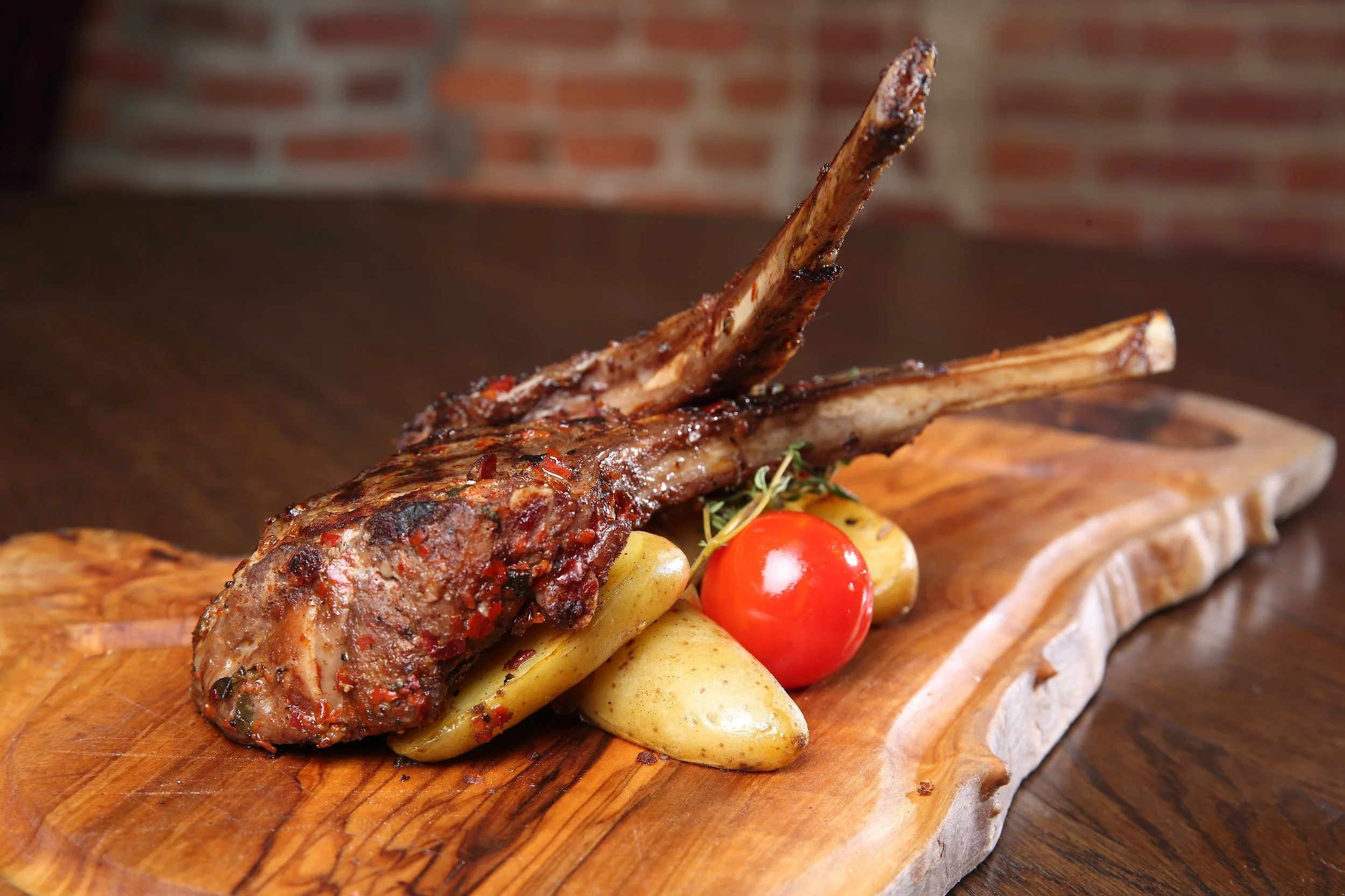 Grilled lamb chops on a wooden serving board with roasted potatoes, cherry tomato, and herbs