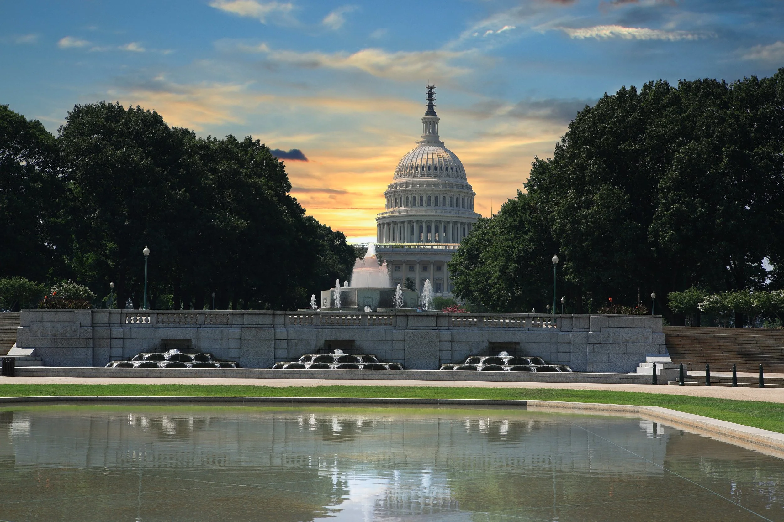 The United States Capitol building in Washington, D.C., at sunset, with fountains and trees in the foreground.
