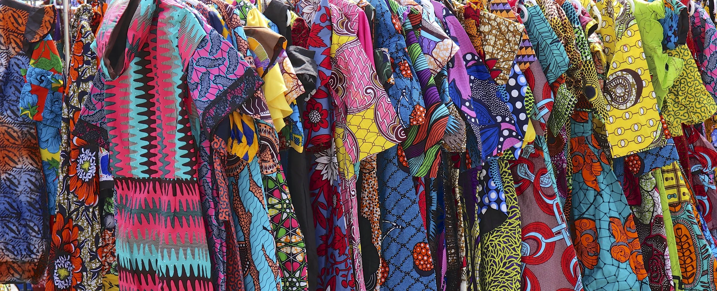 Colorful, patterned fabric shirts hanging on racks at a clothing store.