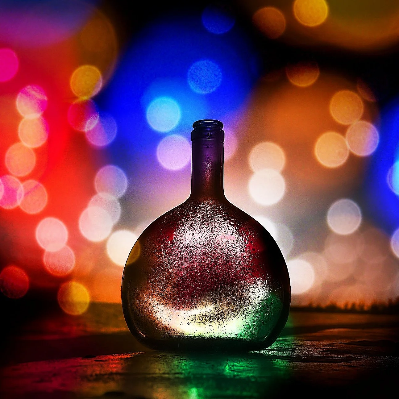 A glass bottle with condensation on it, placed on a wooden surface with colorful bokeh lights in the background.