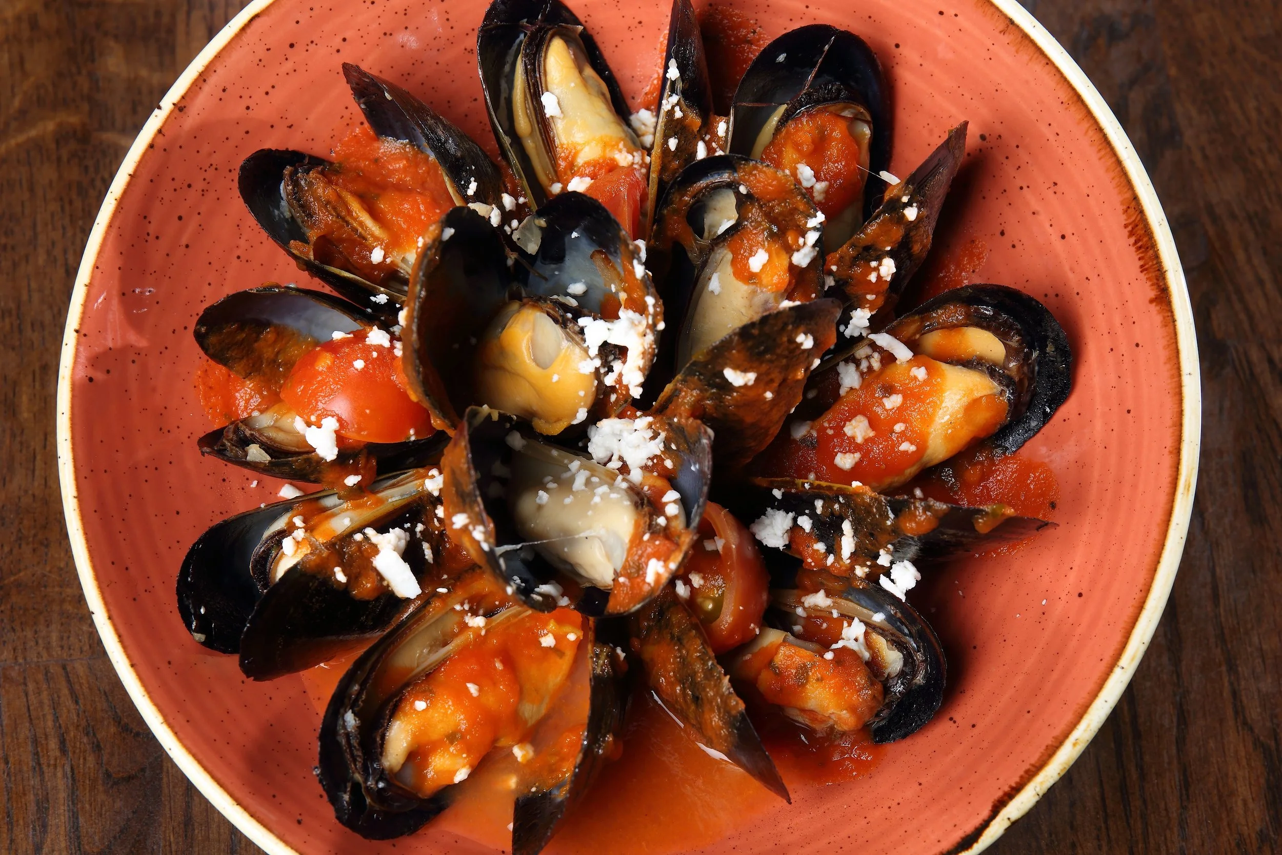 A bowl of cooked mussels topped with tomato sauce and crumbled cheese.