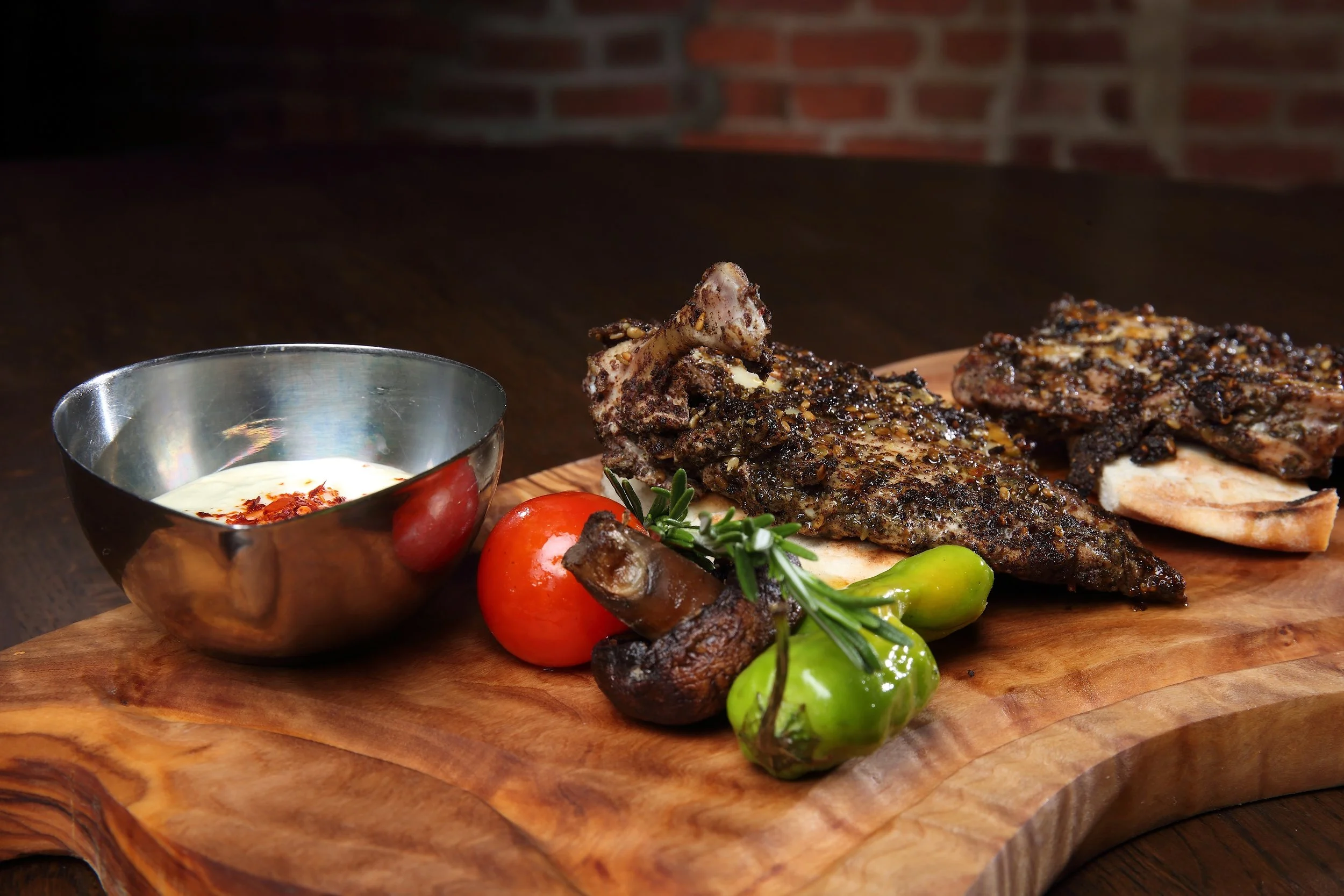 Grilled meat with vegetables and dipping sauce on a wooden cutting board