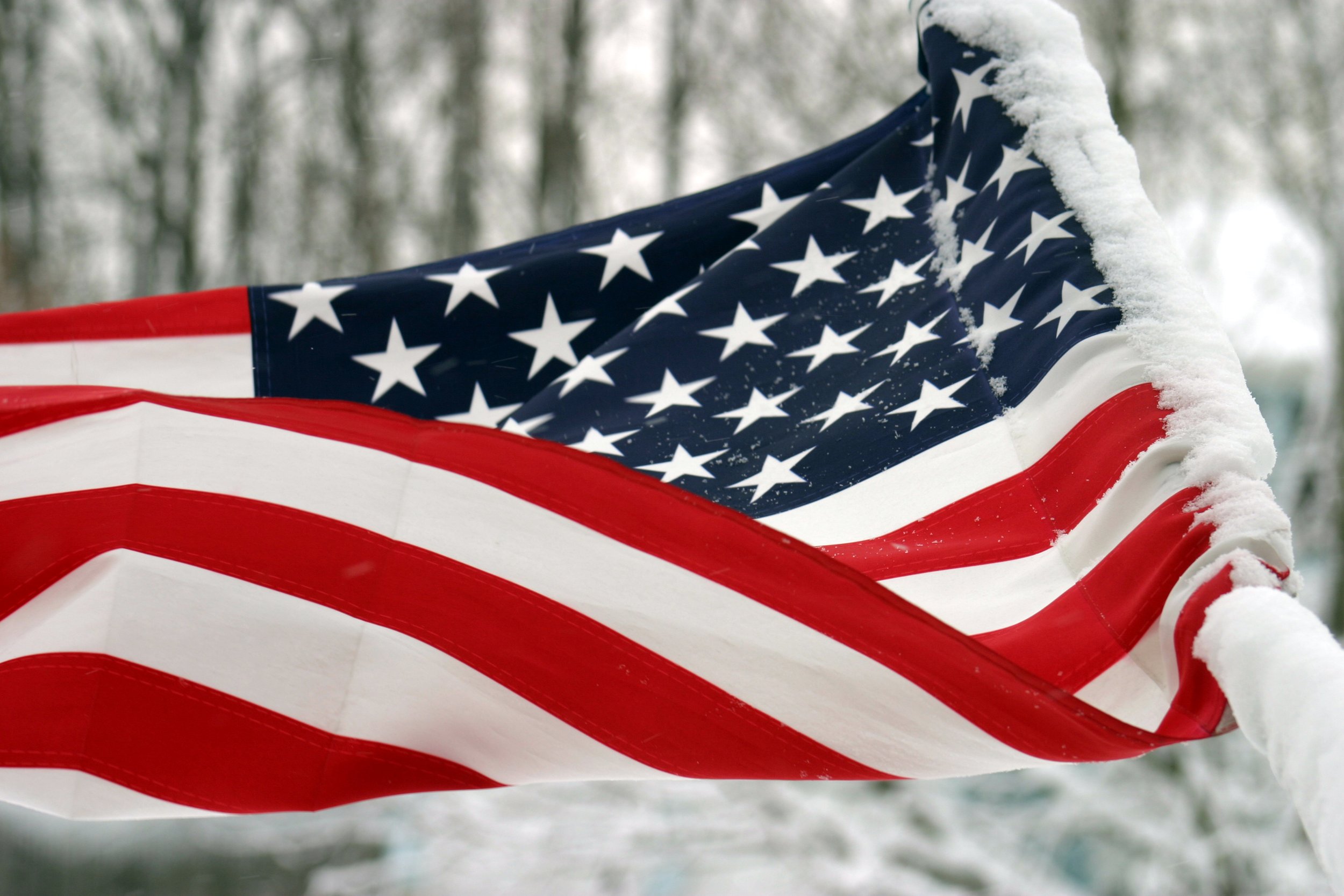 American flag covered in snow, waving outdoors during winter.