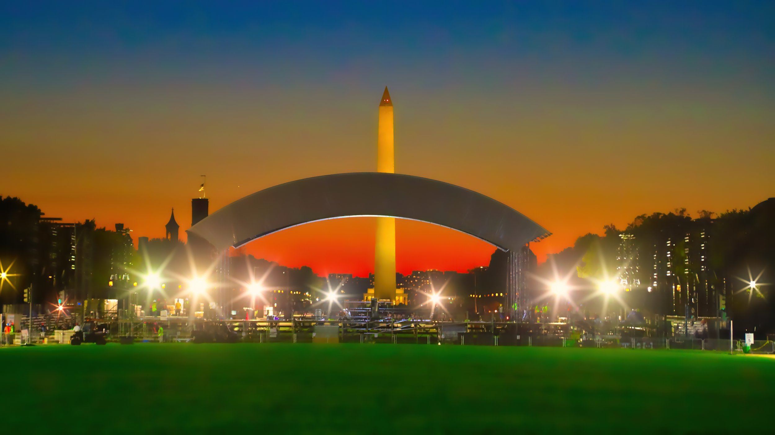 Washington D.C. National Memorial during sunset with the Washington Monument illuminated in the background and a stage with bright lights in the foreground.
