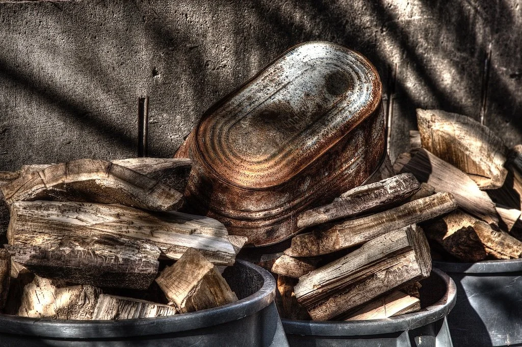Rusty metal lunchbox resting on stacked split firewood with sunlight casting shadows.