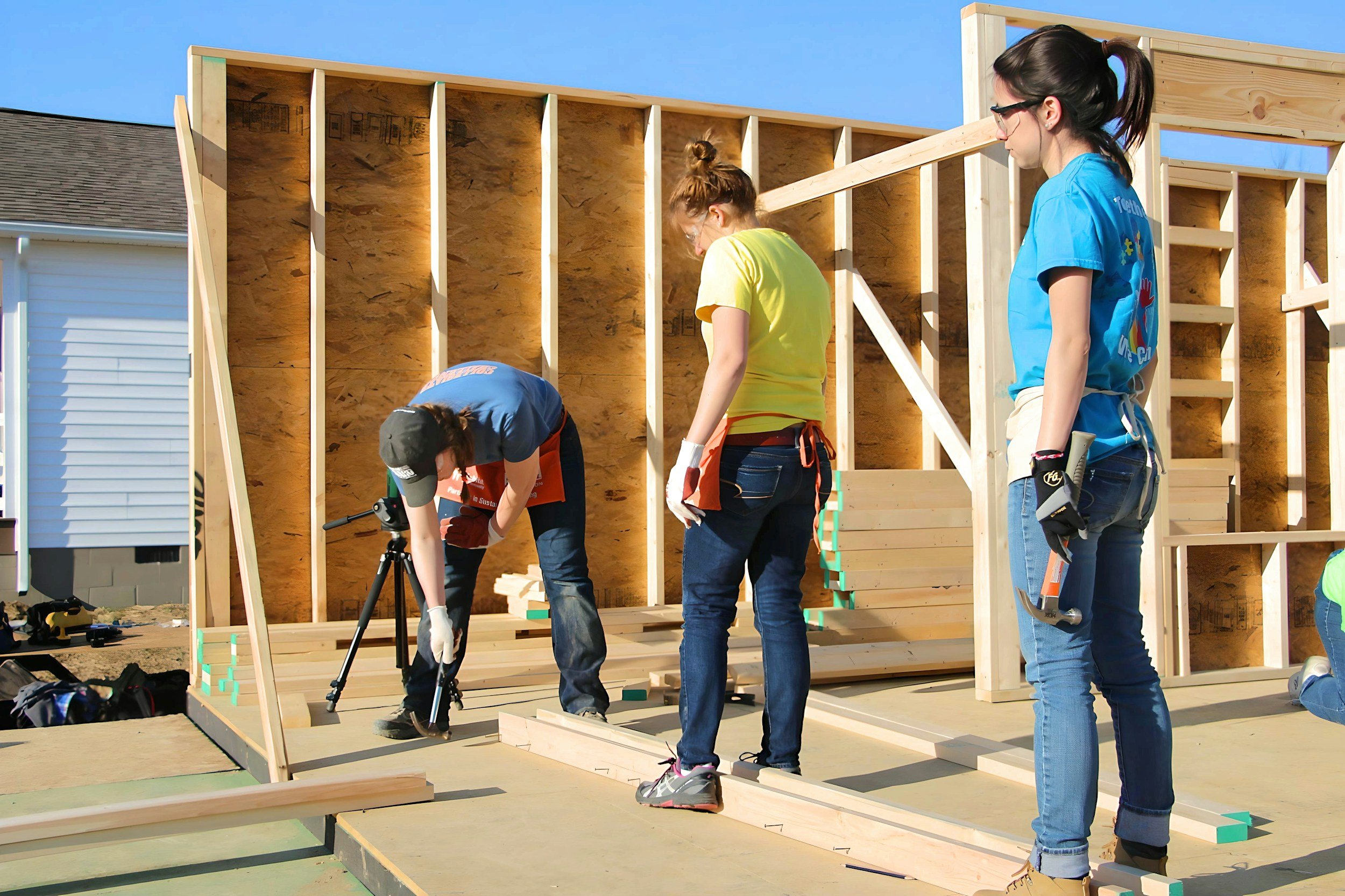 People building a wooden house frame outdoors on a sunny day.