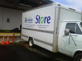 White mobile Habitat store truck parked outside of a building with orange cones nearby.