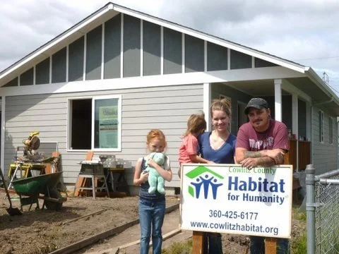 Family at a house construction site holding a Habitat for Humanity sign.