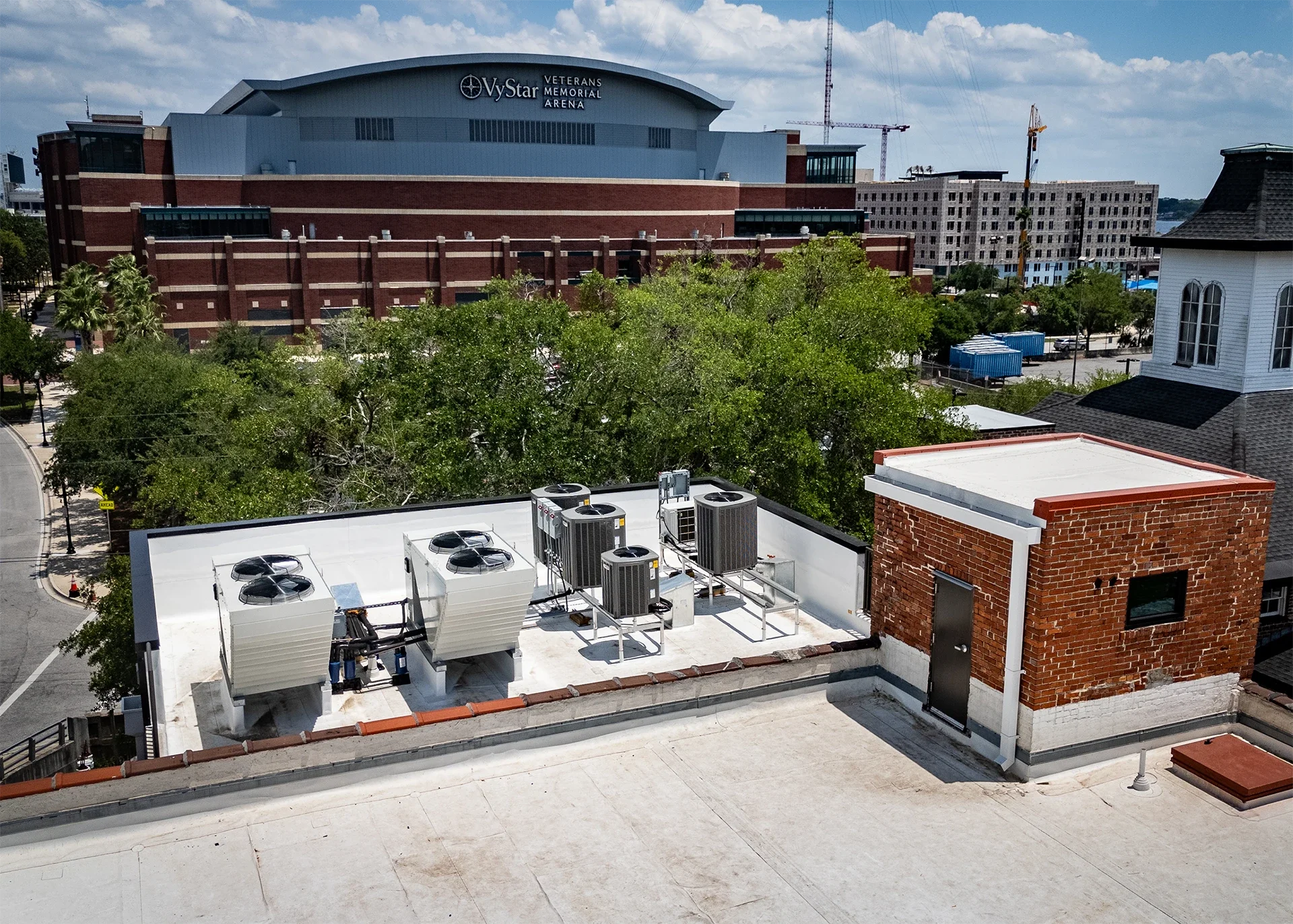 View from a rooftop showing air conditioning units, a small brick structure, and a large building labeled Vystar Veterans Memorial Arena in the background, with trees and other buildings in the distance under a cloudy sky.