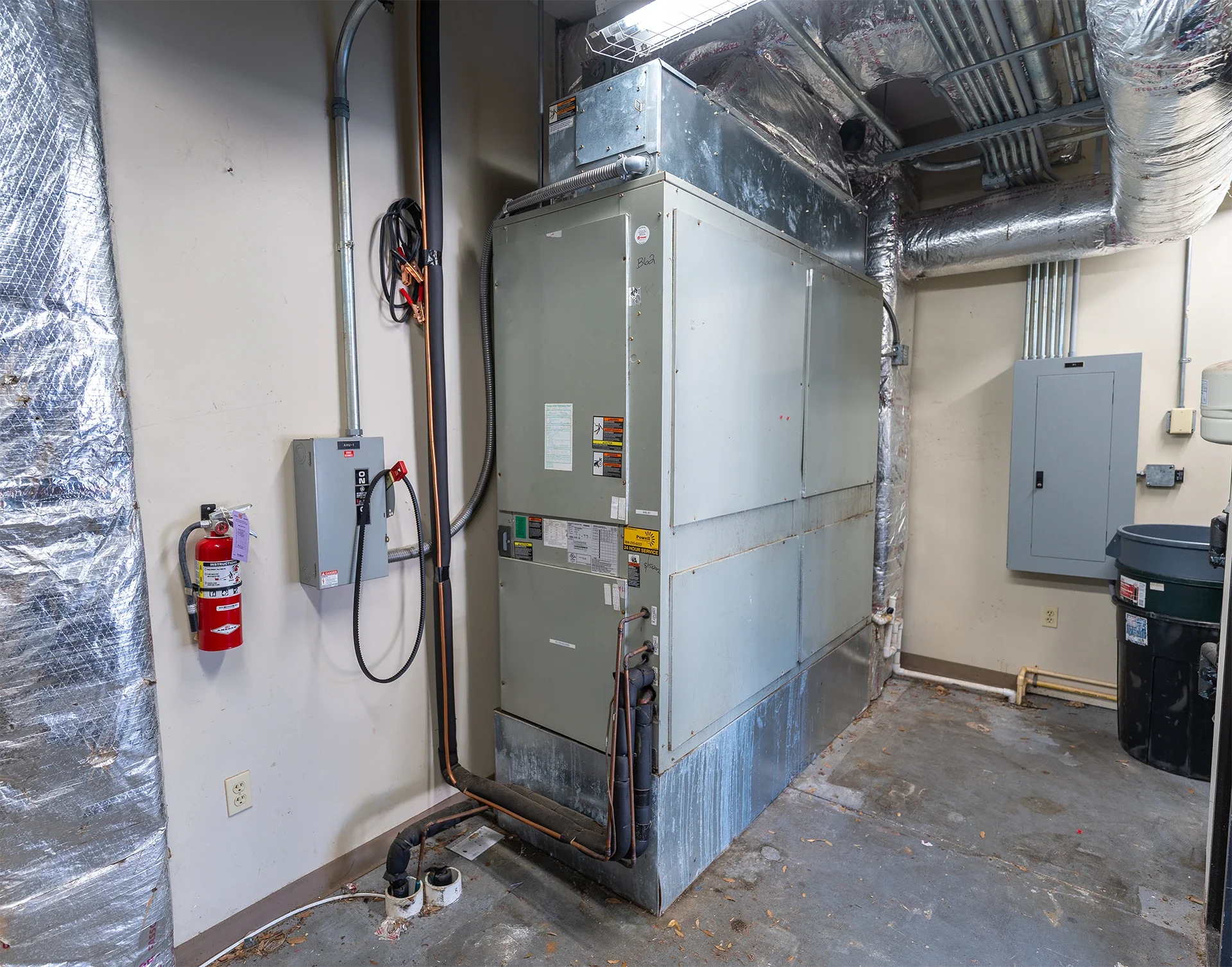 Industrial HVAC unit with ductwork, electrical panels, and fire extinguisher in utility room.