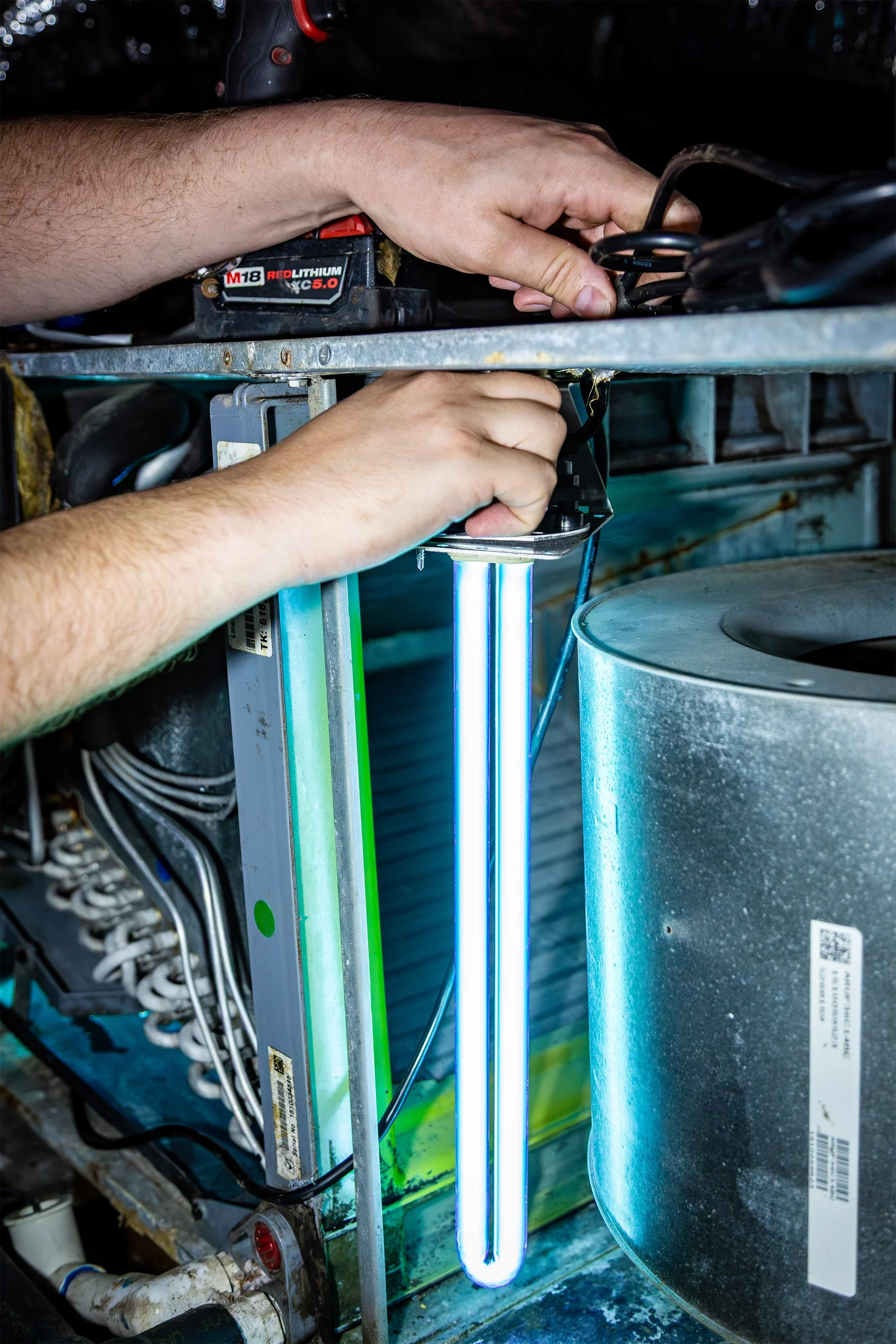 A person working on an industrial machine with an ultraviolet light tube, wiring, and metal components.