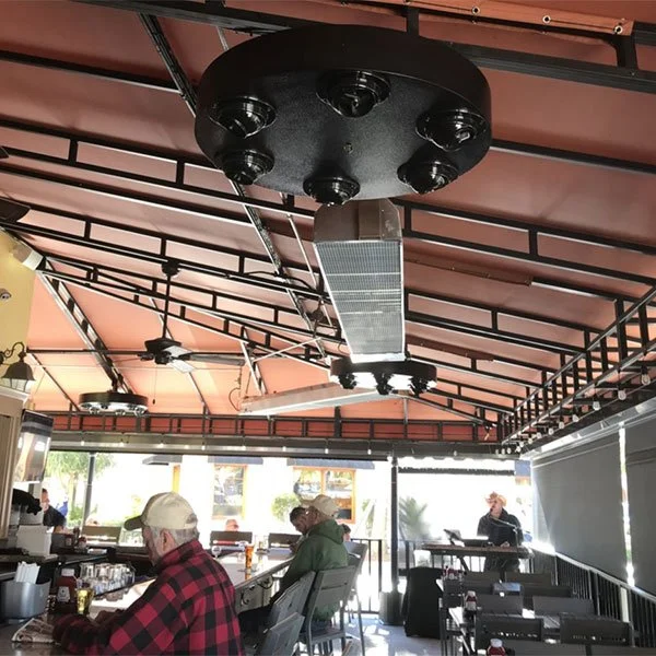 Interior of a restaurant with customers sitting at a bar, large industrial heater hanging from the ceiling, and a ceiling fan.