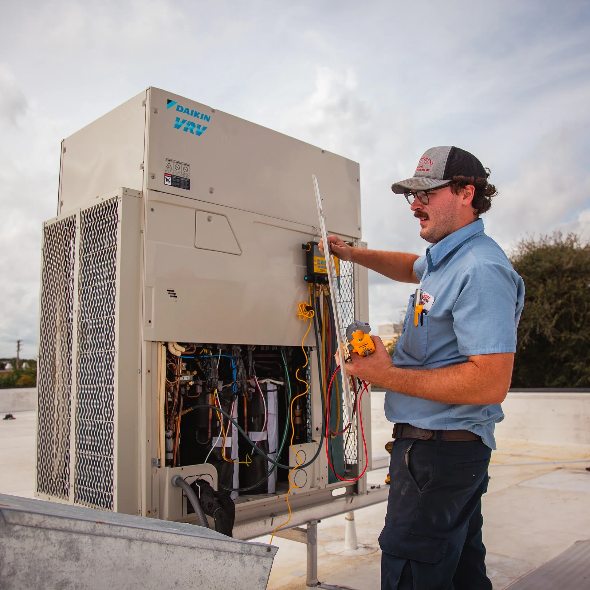 A technician repairing an industrial air conditioning unit on a rooftop, using a digital multimeter.
