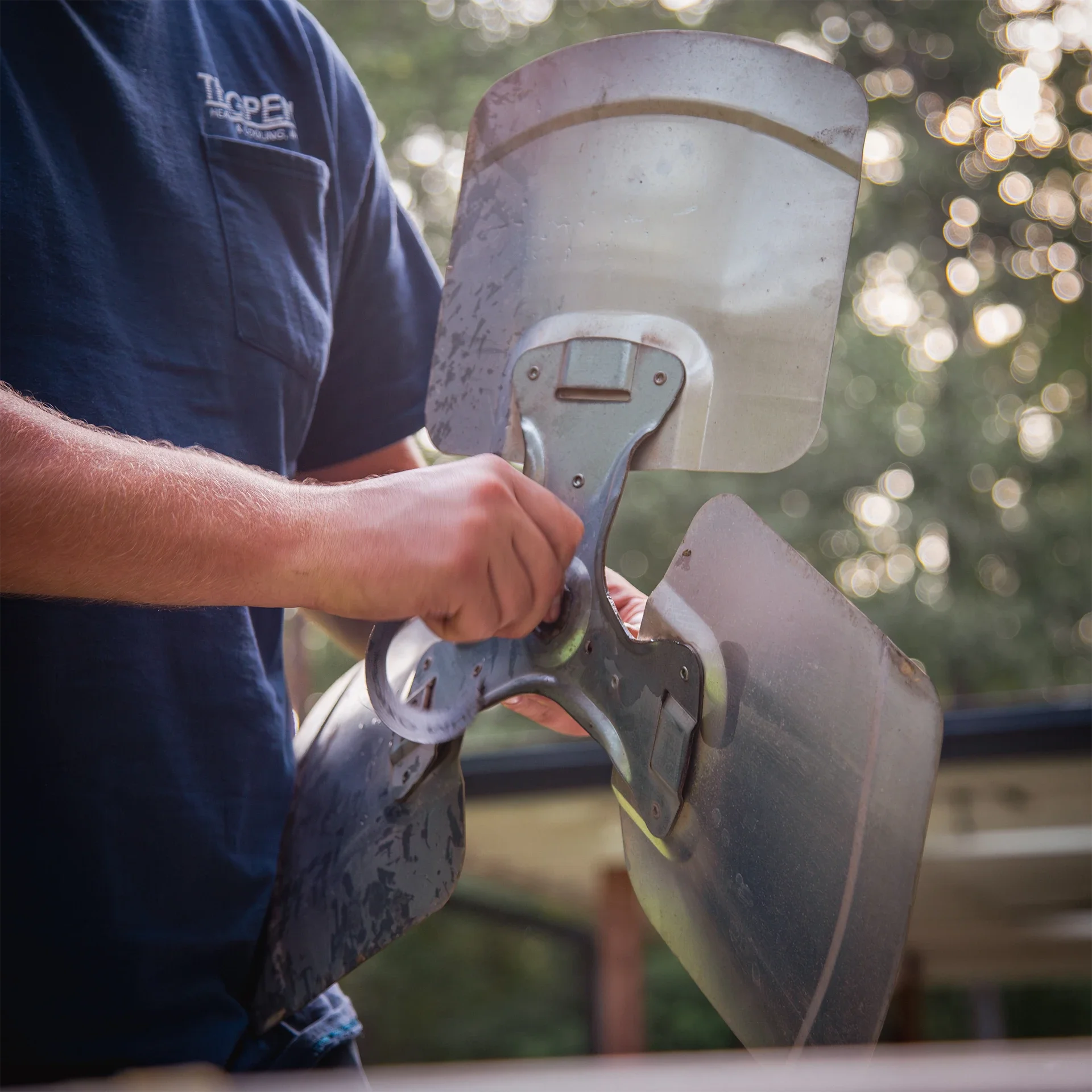 A person holding a metal propeller with two blades, likely for a small aircraft or drone, in an outdoor setting during sunset.