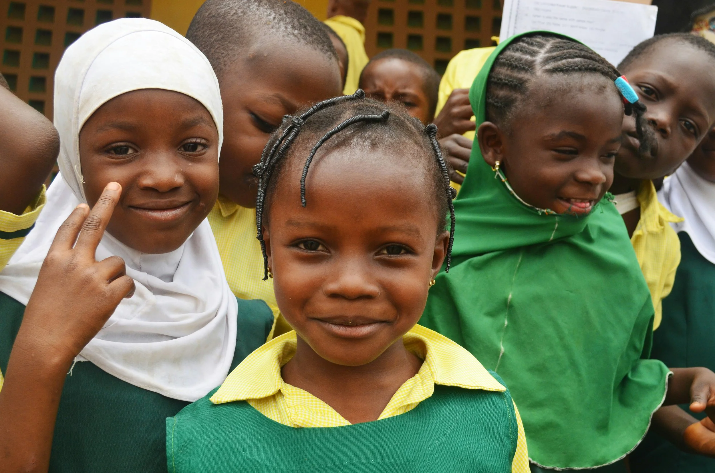 Group of children in school uniforms, smiling and posing for a photo outdoors.
