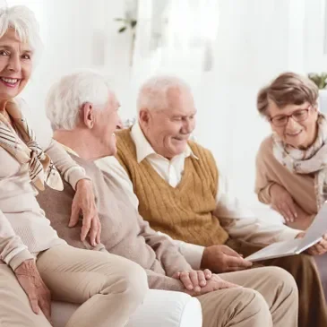 Four elderly people sitting together in a bright room, smiling and engaging in conversation.