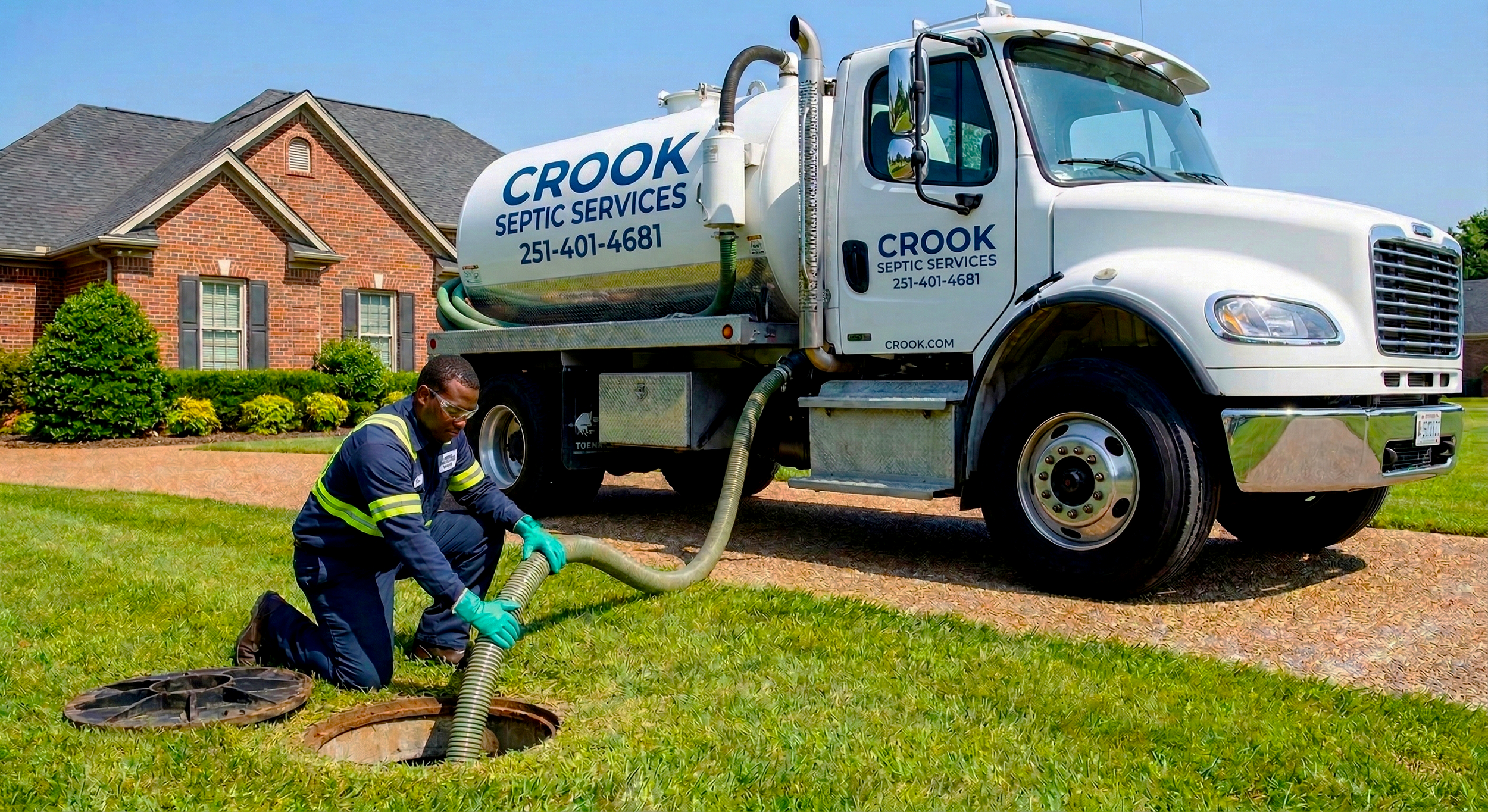 A technician from Crook Septic Services kneeling on grass, handling a large hose connected to a septic truck in front of a red brick house with a well-manicured lawn and bushes.