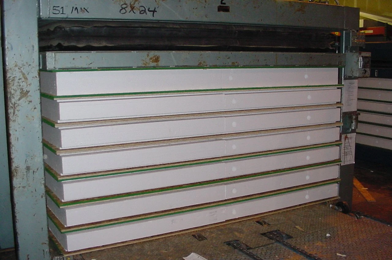 SIP panel assembly line showing OSB facings being bonded to foam core under pressure.