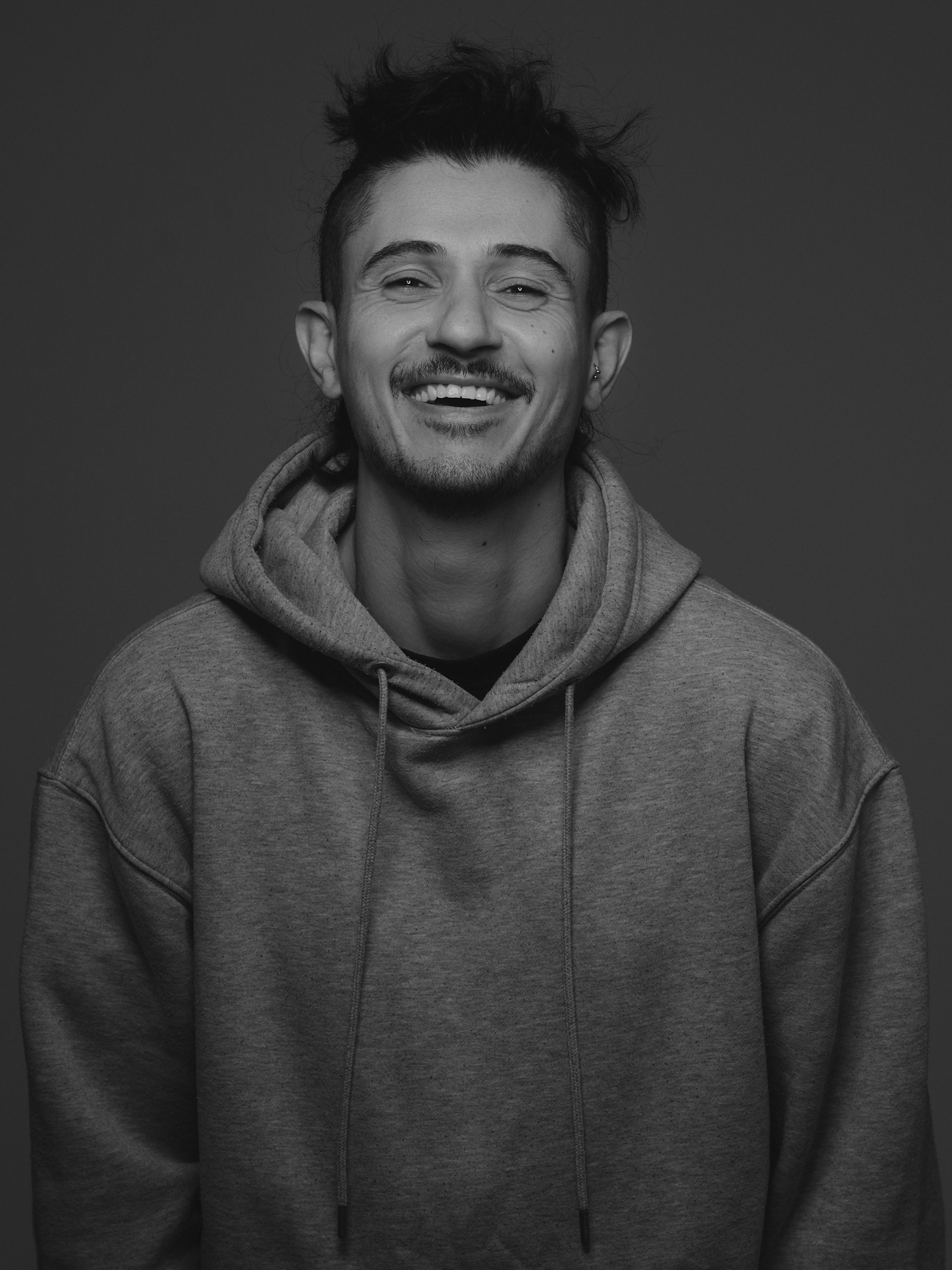 Black and white portrait of a man smiling, wearing a hoodie.