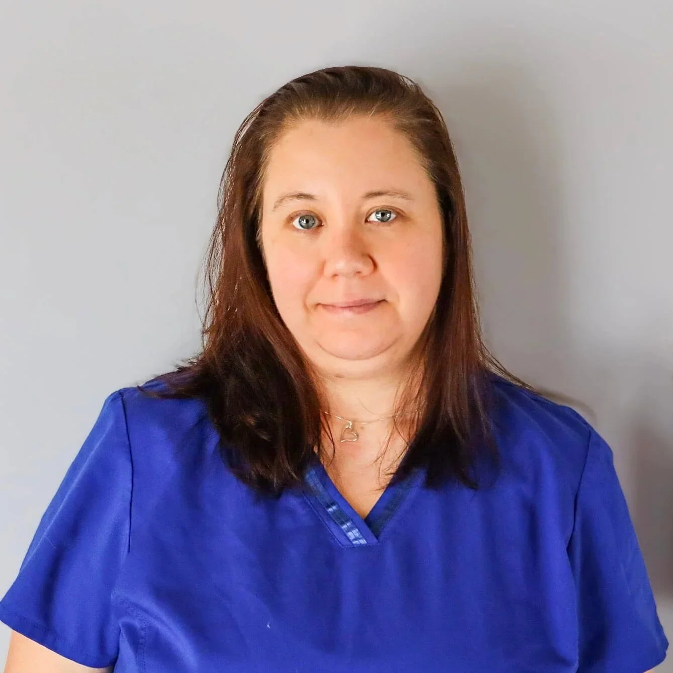 Portrait of a woman with shoulder-length brown hair wearing a blue medical uniform in front of a light gray background.