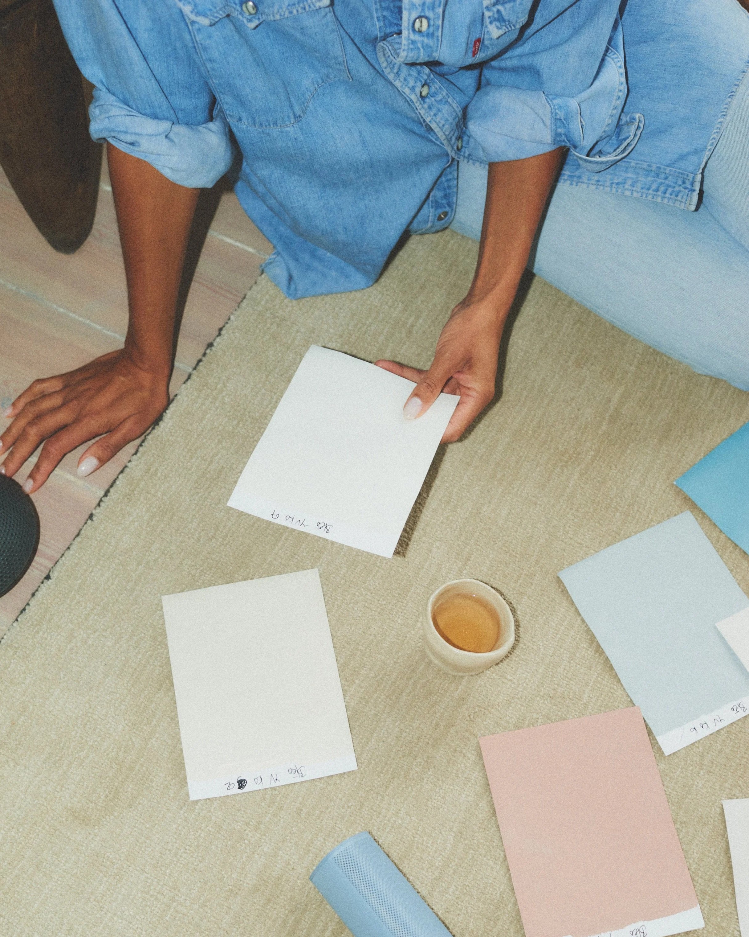 Yvonne Koné sitting on the floor, surrounded by and working with hand mixed color samples from her exclusive wall color collection for Bleō. The image captures the natural hands on curated color selection process.