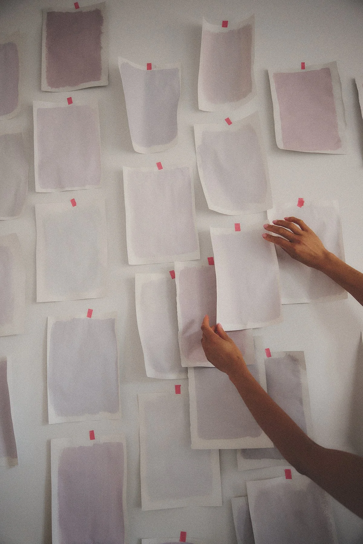 Custom made color samples for a spatial design client. Hands pinning and arranging bespoke color sheets on a wall to visualize a new interior environment by Yvonne Koné.