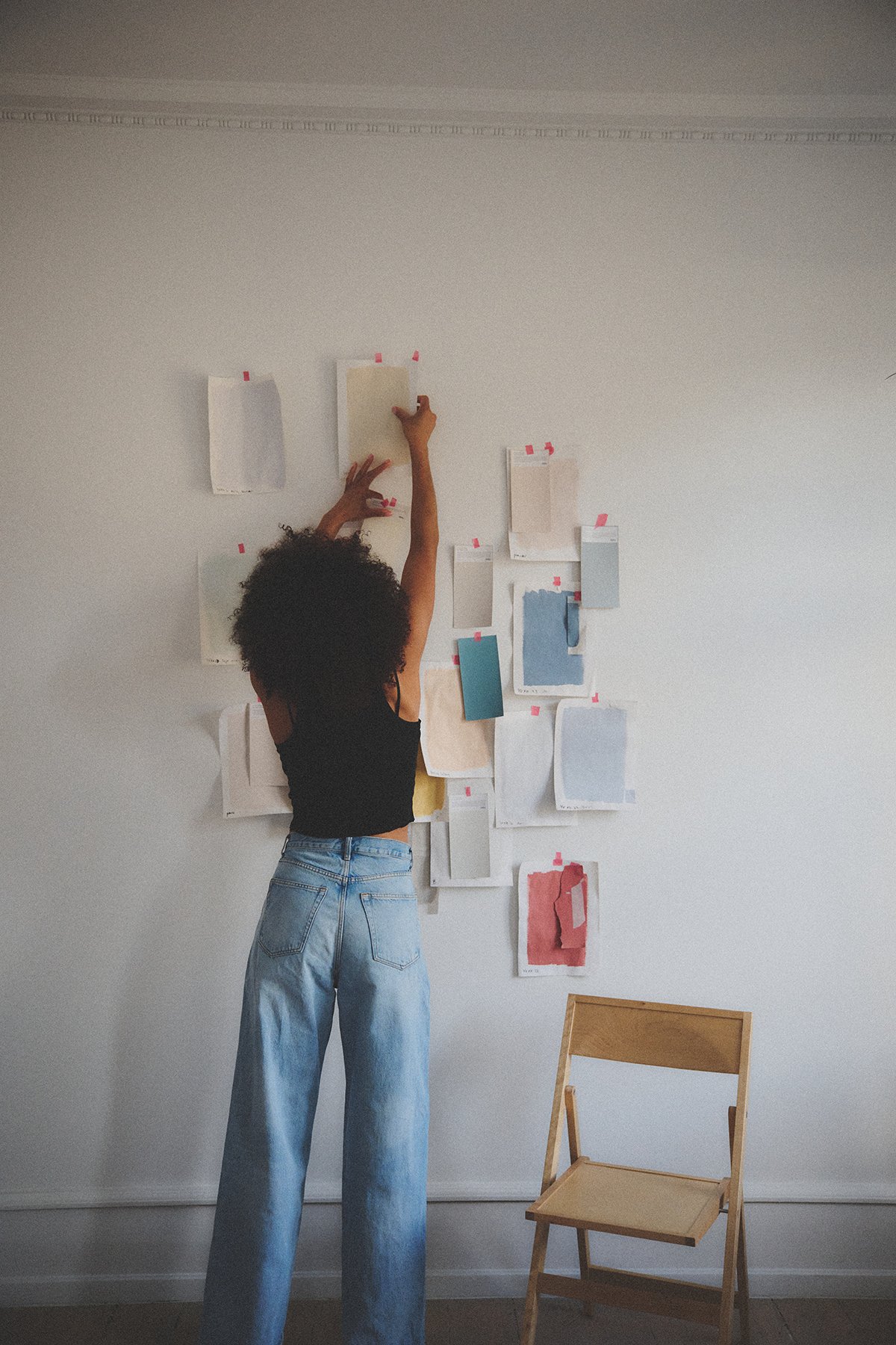 Yvonne Koné pins custom made color samples to the wall in her Copenhagen apartment and studio. Hands pinning and arranging bespoke color sheets to visualize a new interior environment.