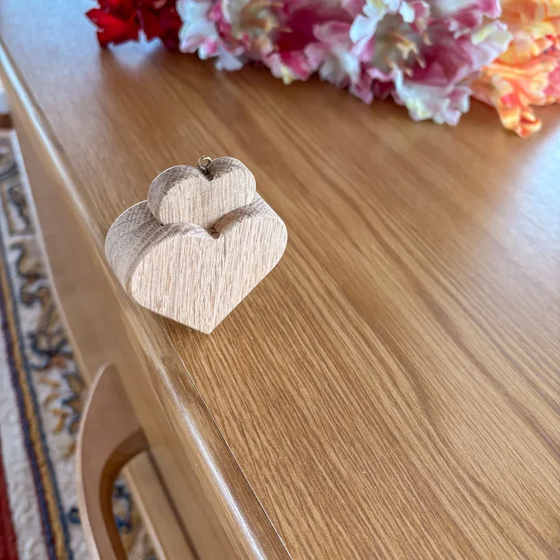 Houten hartvormige en bloemvormige decoraties op een houten uitvaartkist met bloemen in de achtergrond.