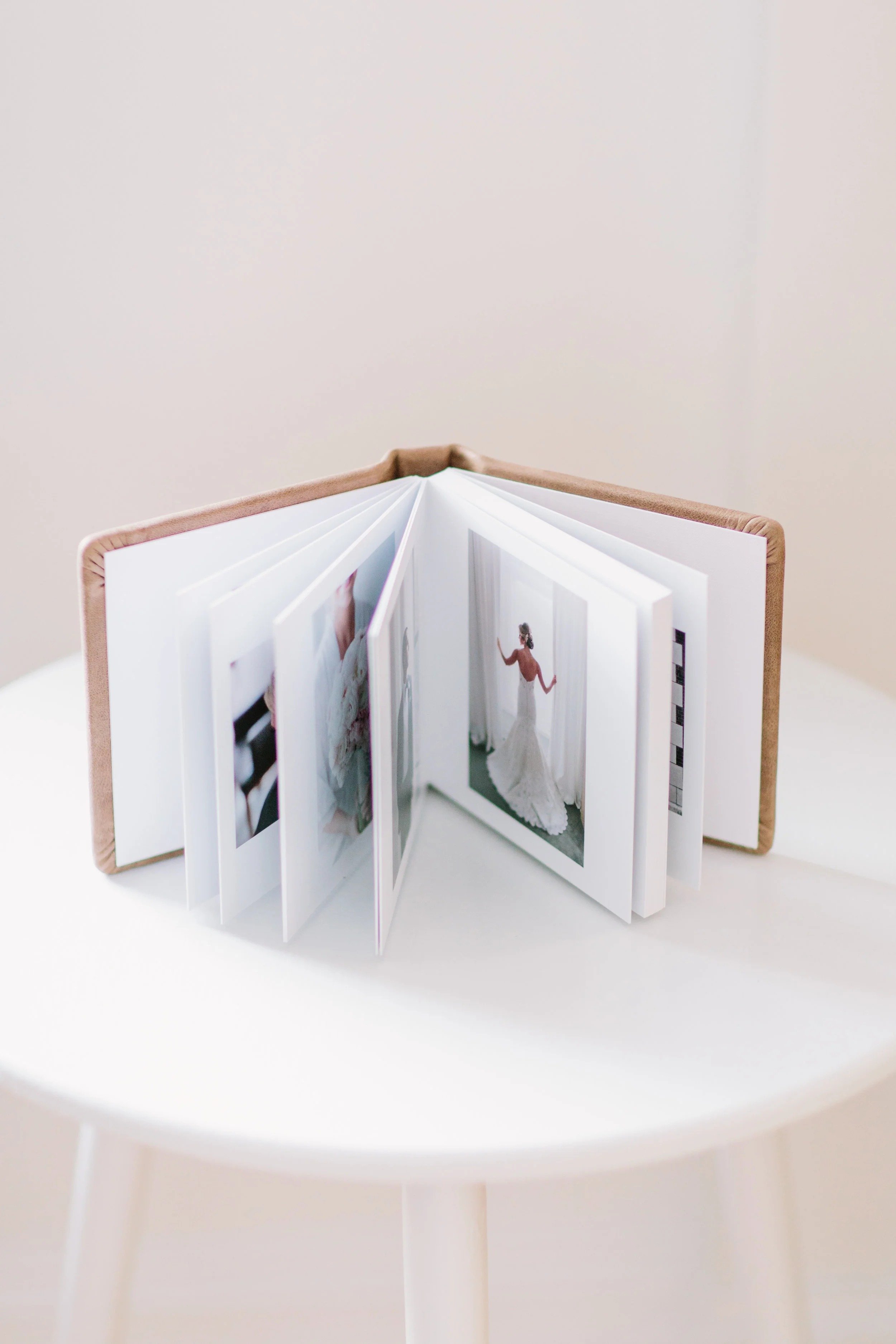 Open photo album with photographs, placed on a white table, bare wall in background.
