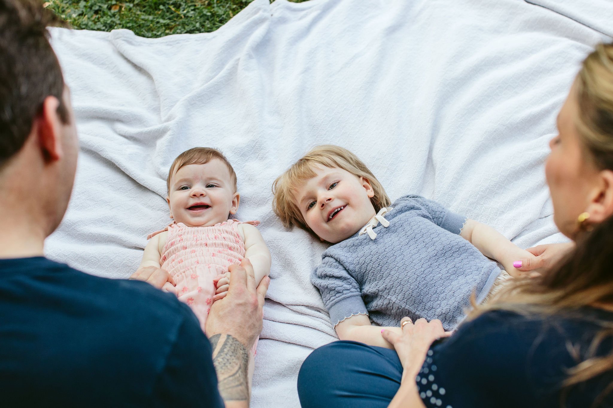 candid photo of two young children laying on a blanket smiling at their parents
