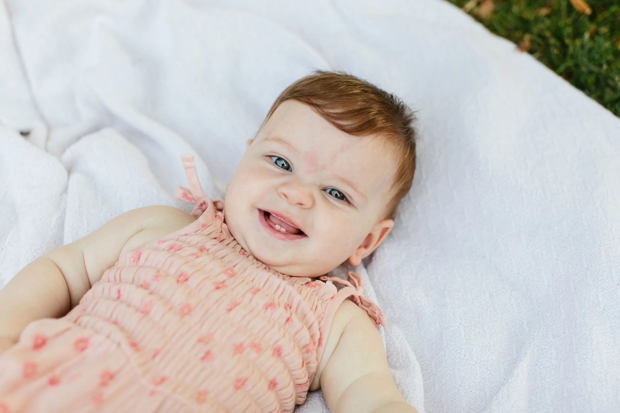 Baby laying on a white blanket, smiling at the camera