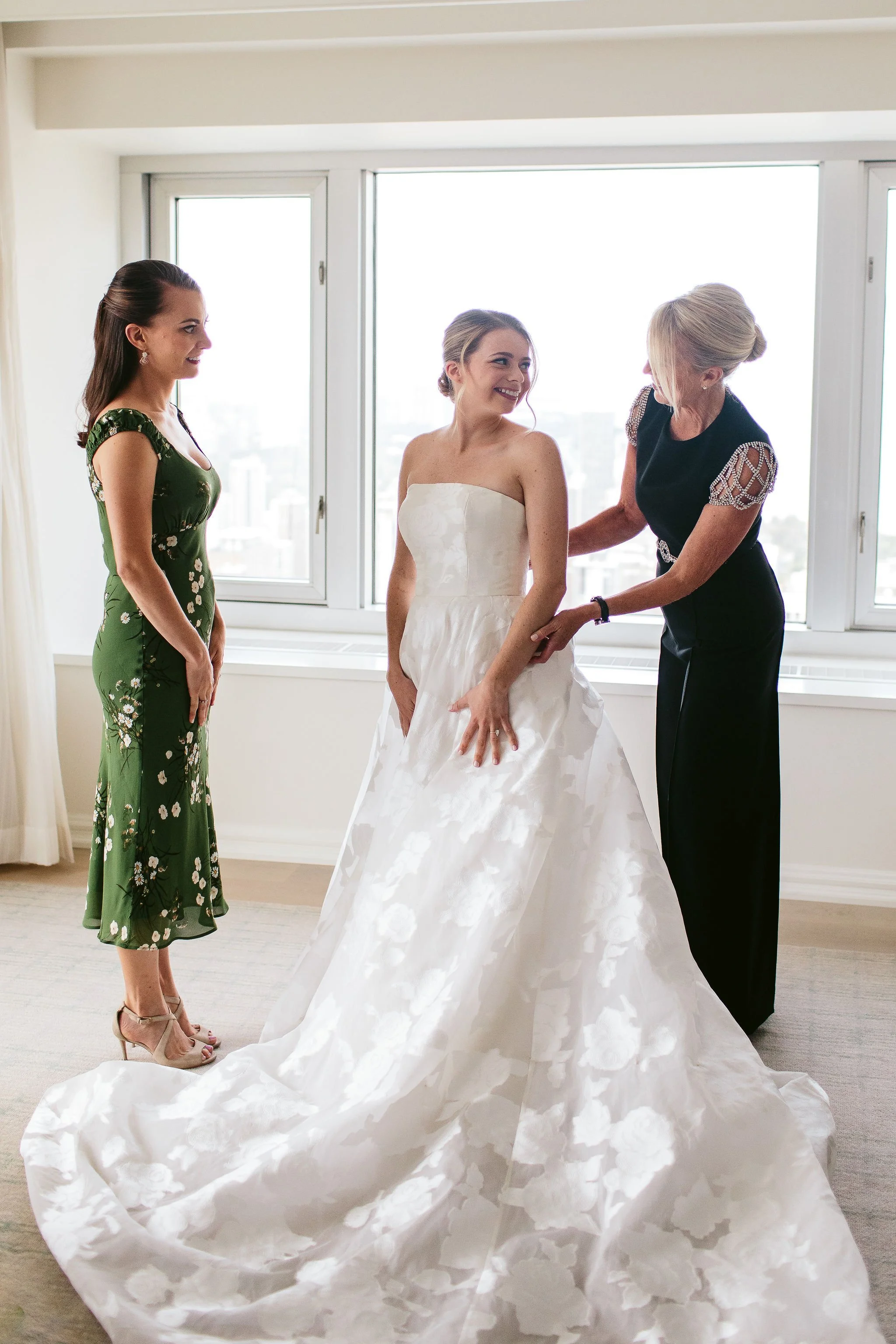 bride putting on dress with mother and sister
