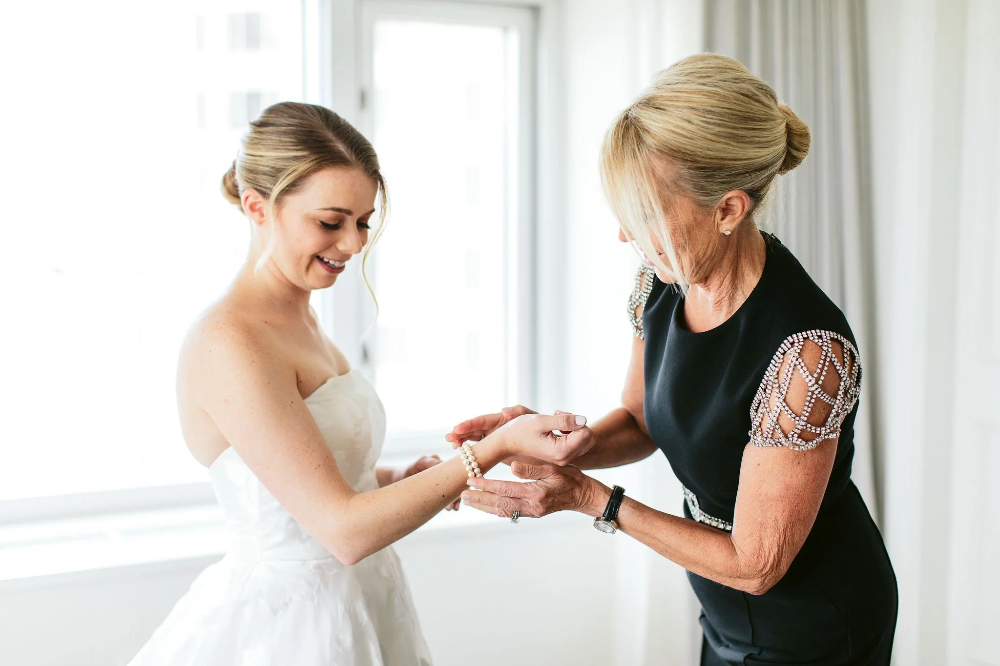 mother putting on bride's jewelry