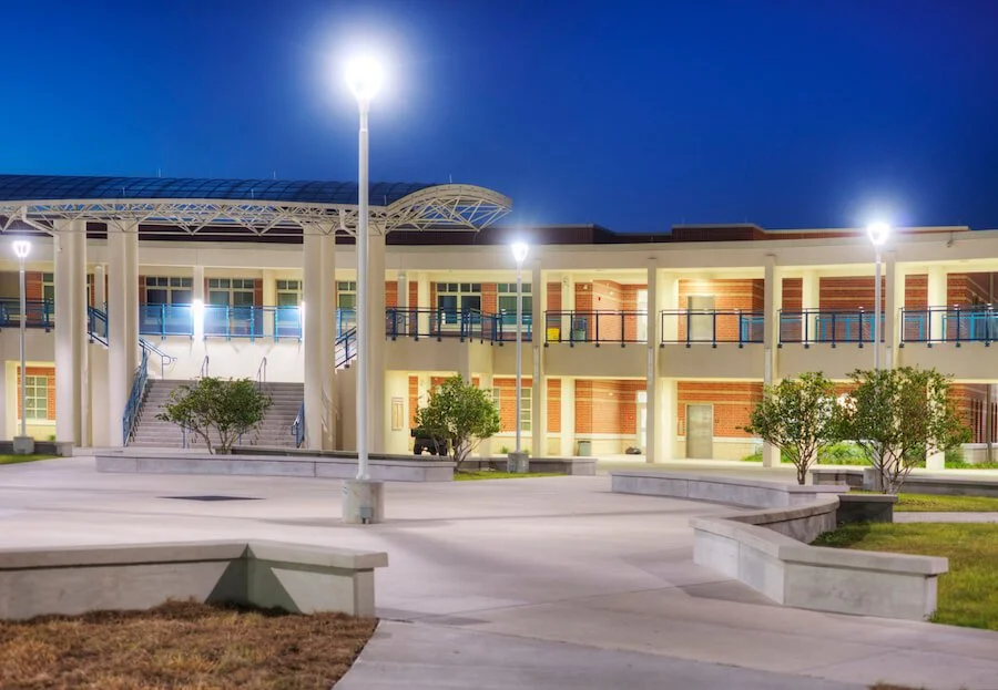 Exterior of a school at night with bright lights in the courtyard and on the building